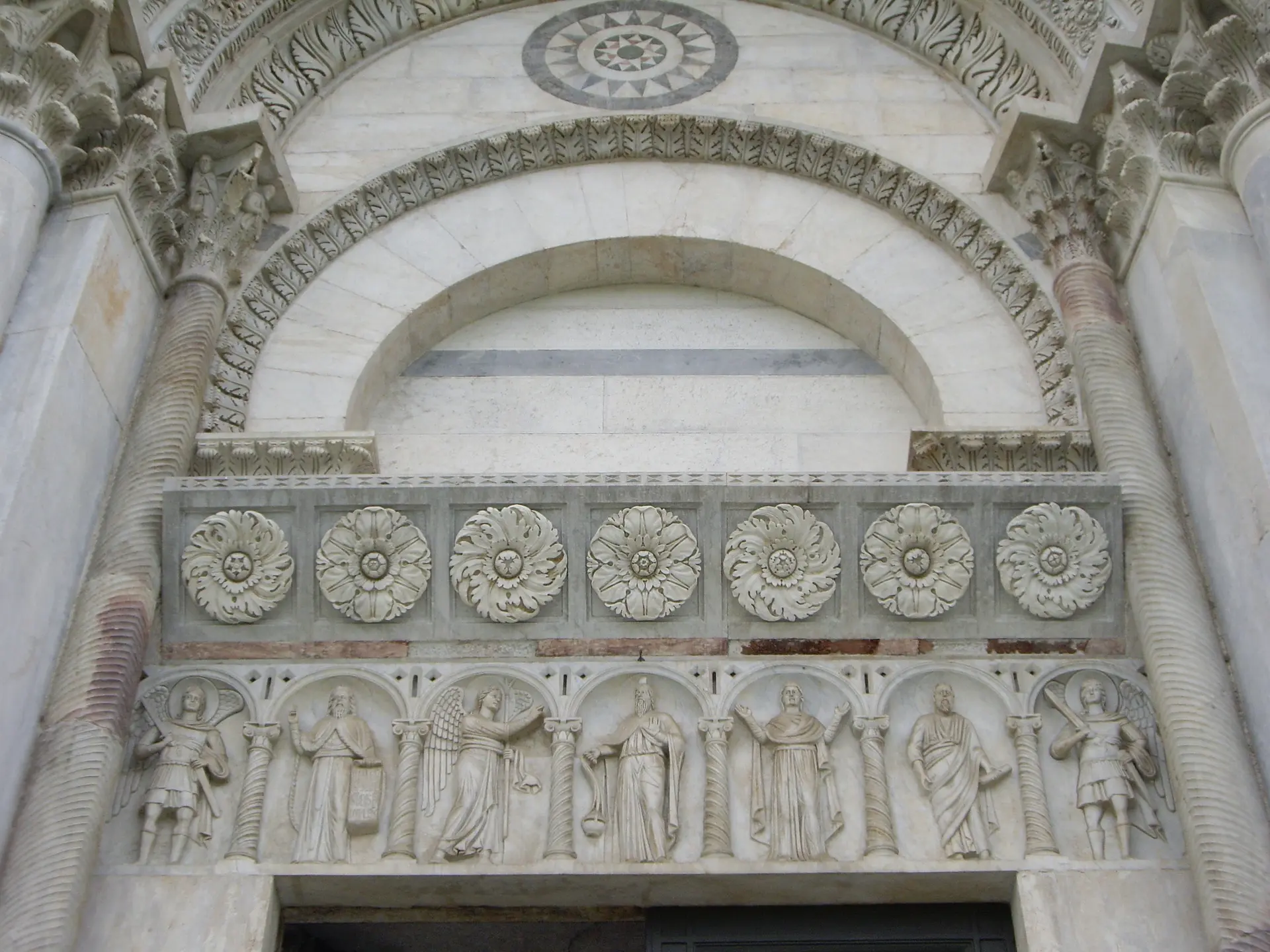 A carved marble frieze of saints and rosettes running above a cathedral doorway in Pisa