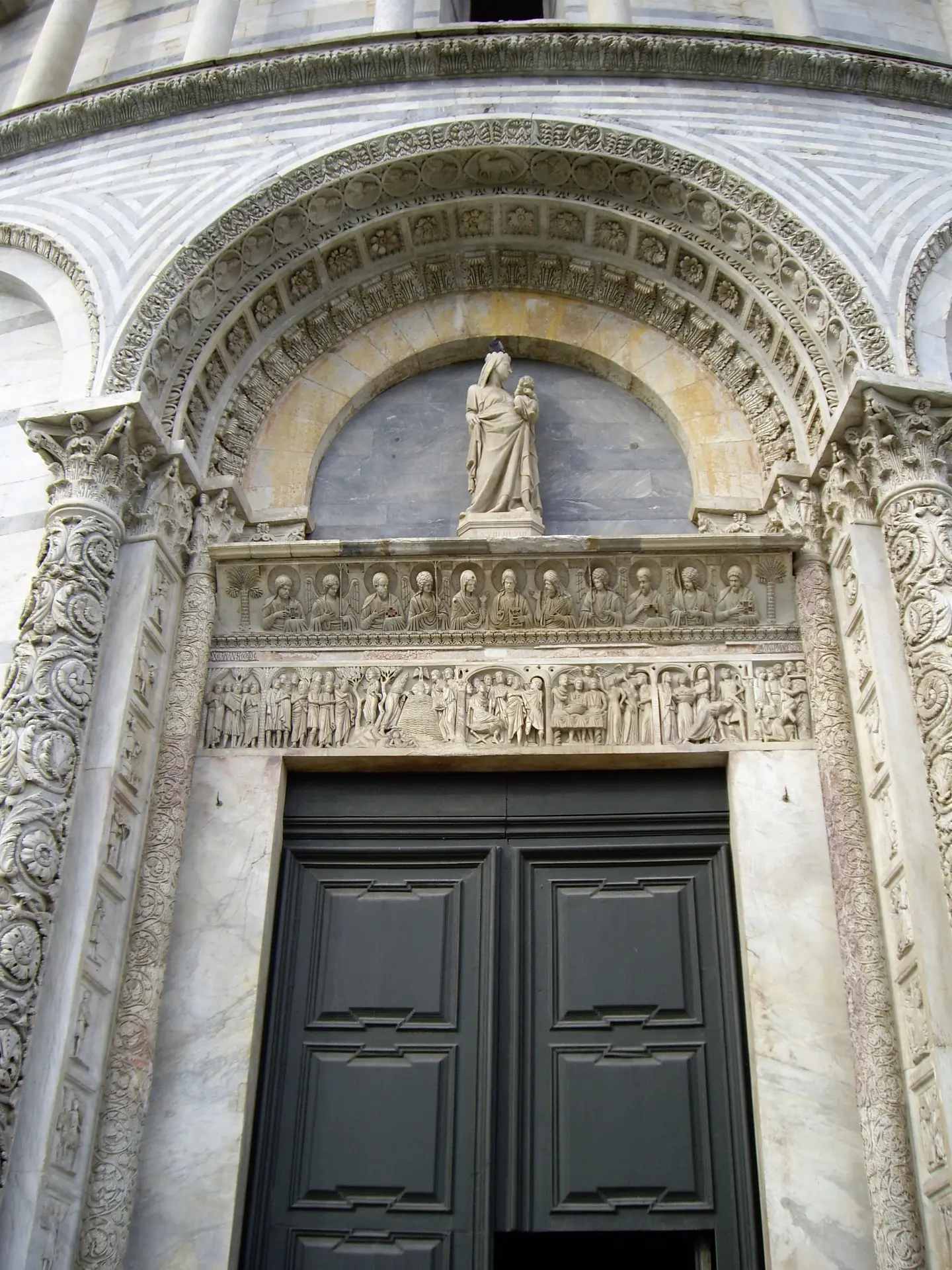 A carved marble portal of Pisa cathedral with a statue in the lunette above the doors