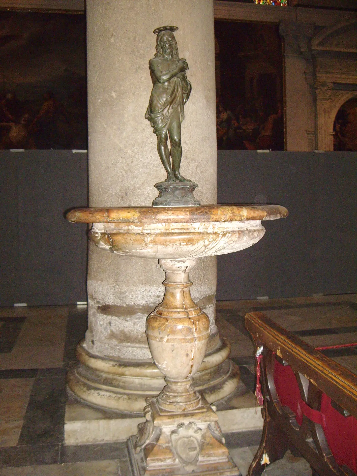A marble holy water stoup with a bronze figure standing on it in Pisa cathedral