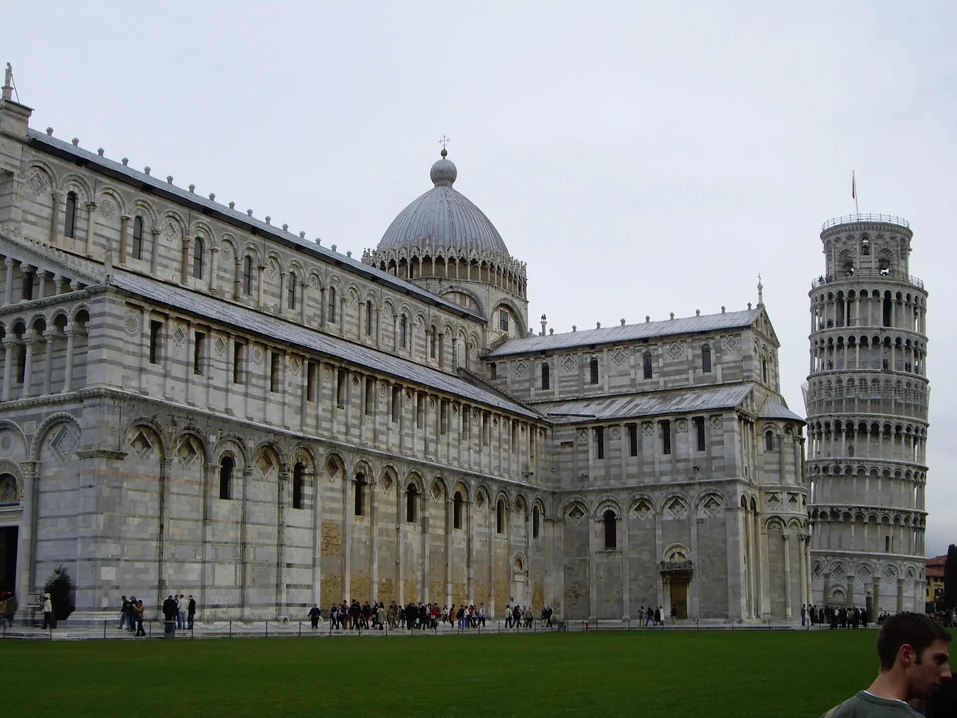 The long marble flank of Pisa cathedral leading to the leaning tower behind it