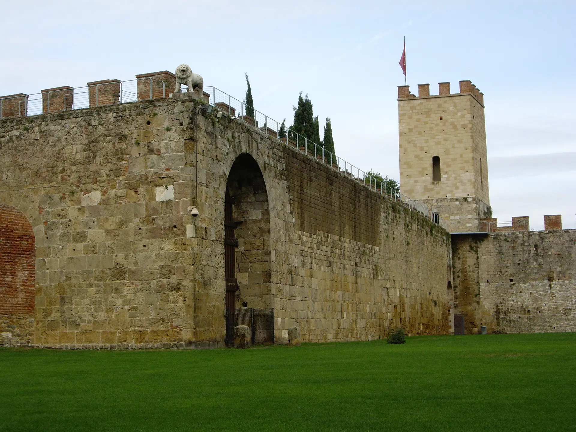 The medieval walls of Pisa with a gate arch and tower above a strip of lawn