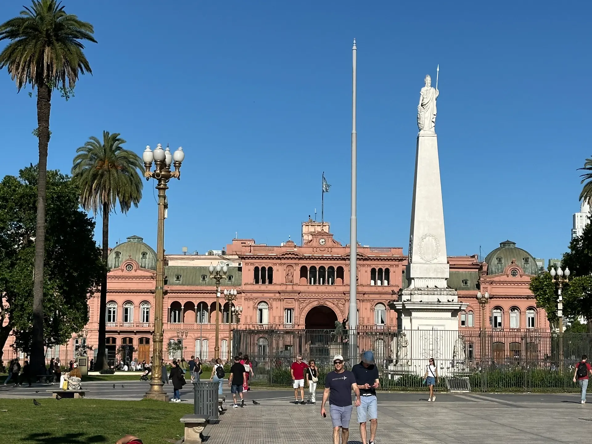 The Casa Rosada across Plaza de Mayo with the Piramide de Mayo and palm trees.