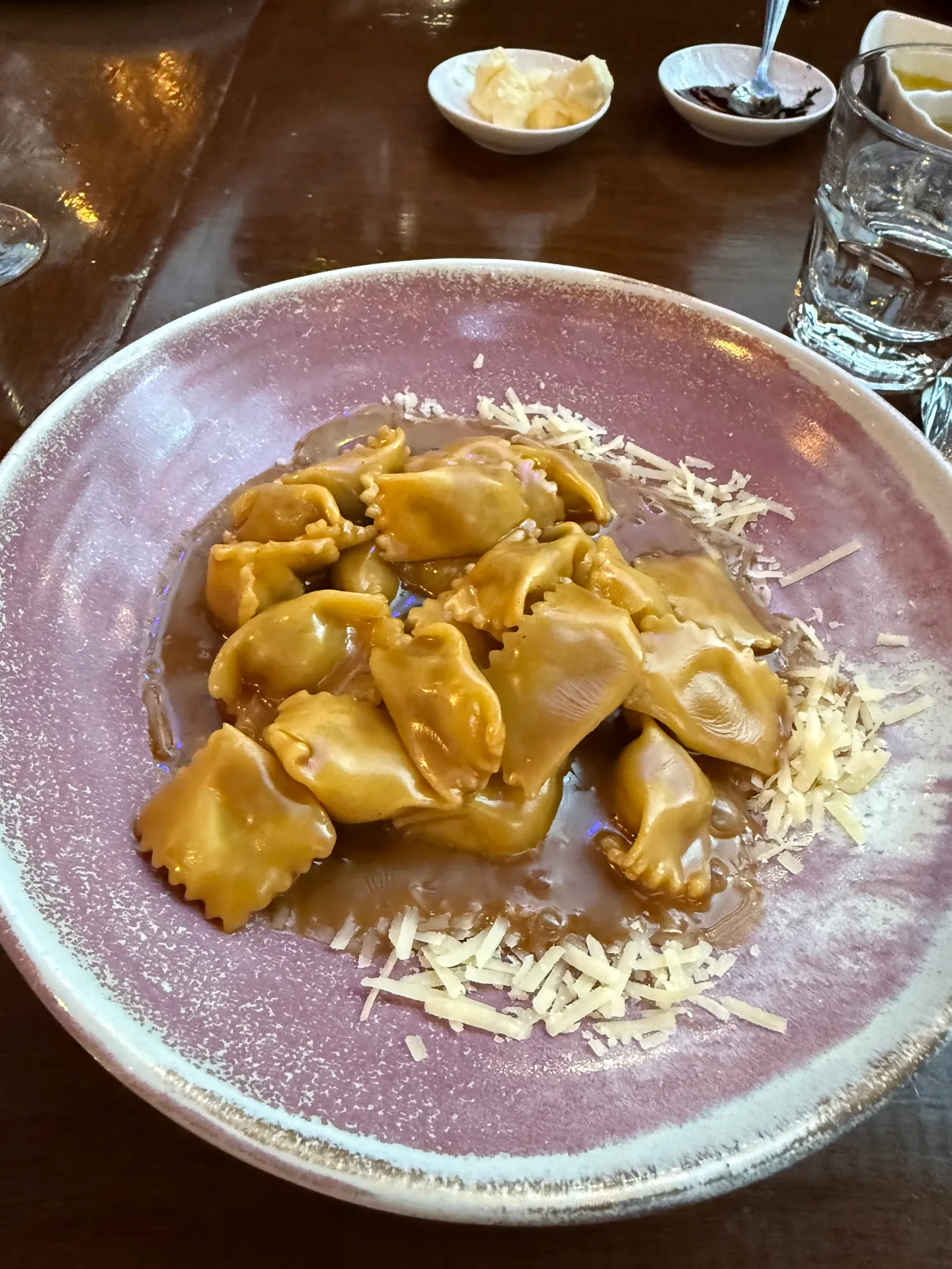 Small pinched filled pasta parcels in a brown sauce with grated cheese on a mauve plate.