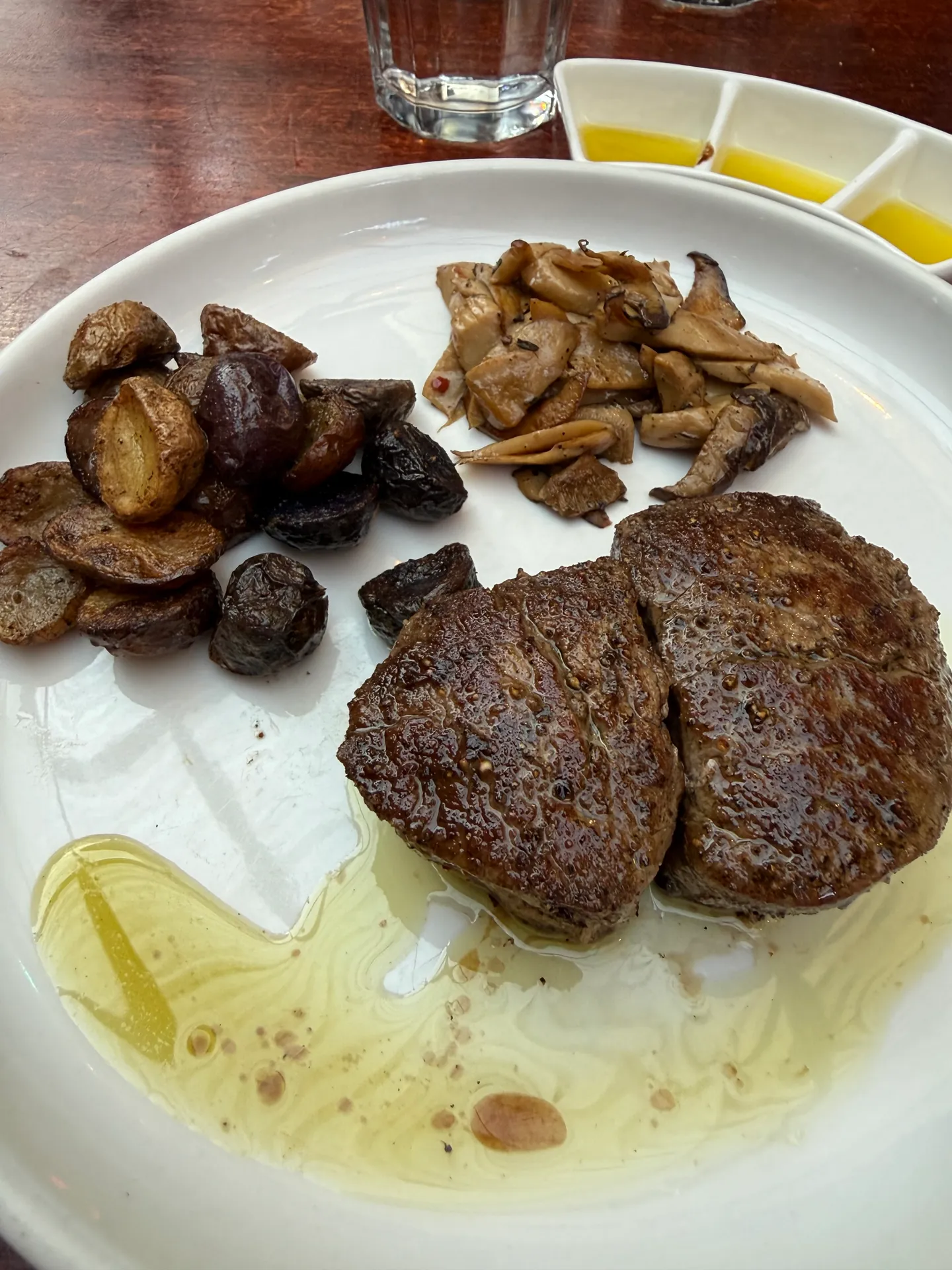 Two seared beef tenderloin medallions with roasted potatoes and mushrooms on a white plate.