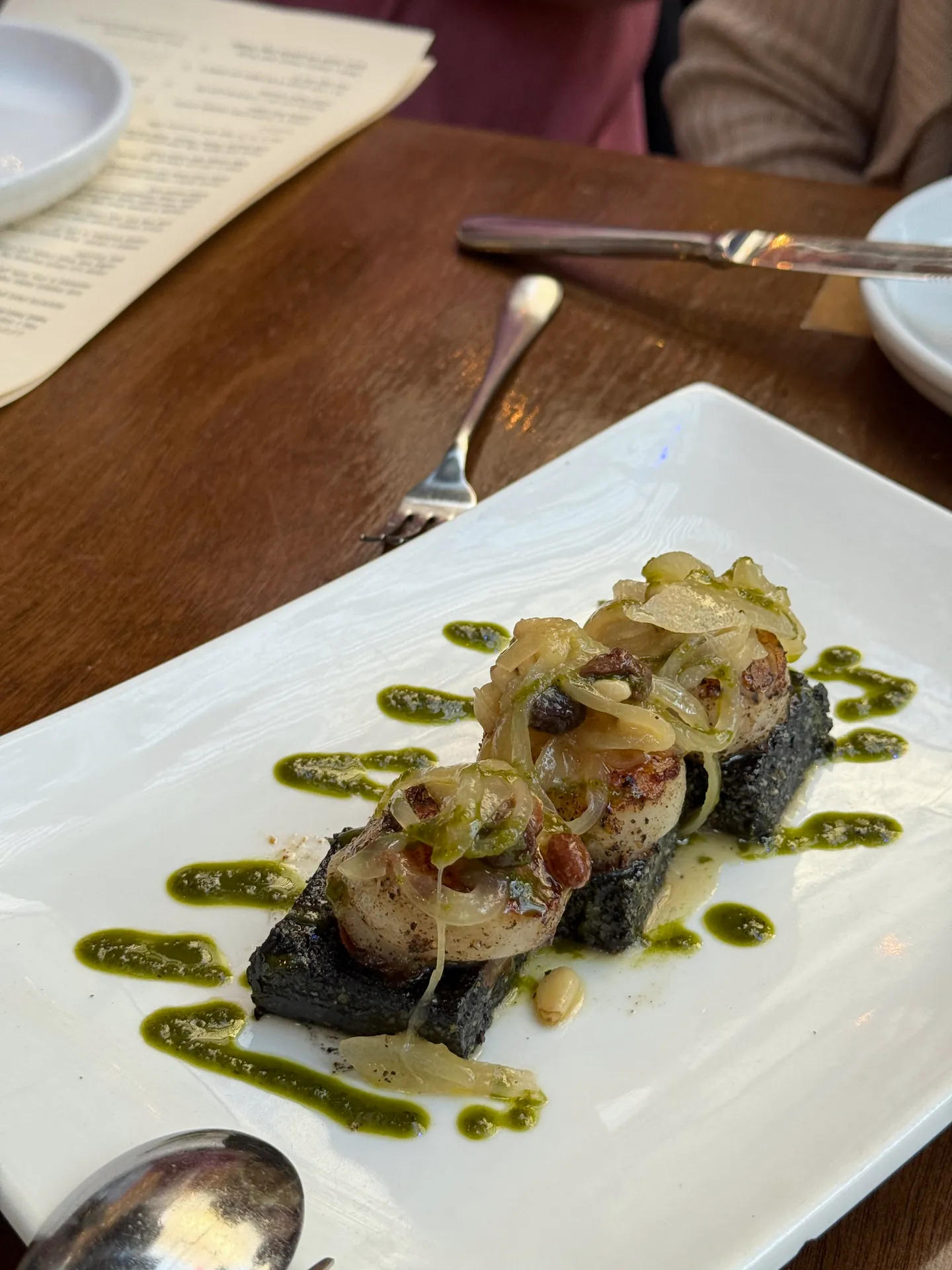 Seared scallops on a black squid-ink polenta cake with onions and green herb oil.