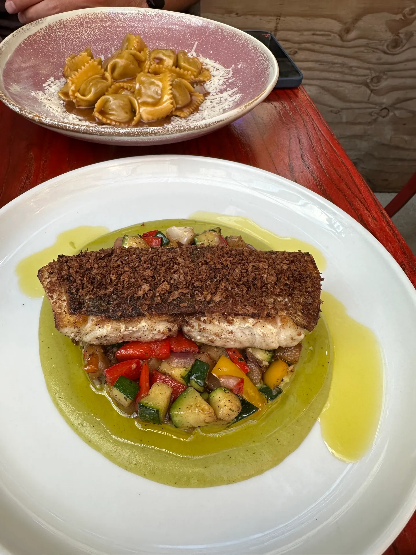 A crusted fillet of fresh white fish over diced zucchini and peppers in green oil.