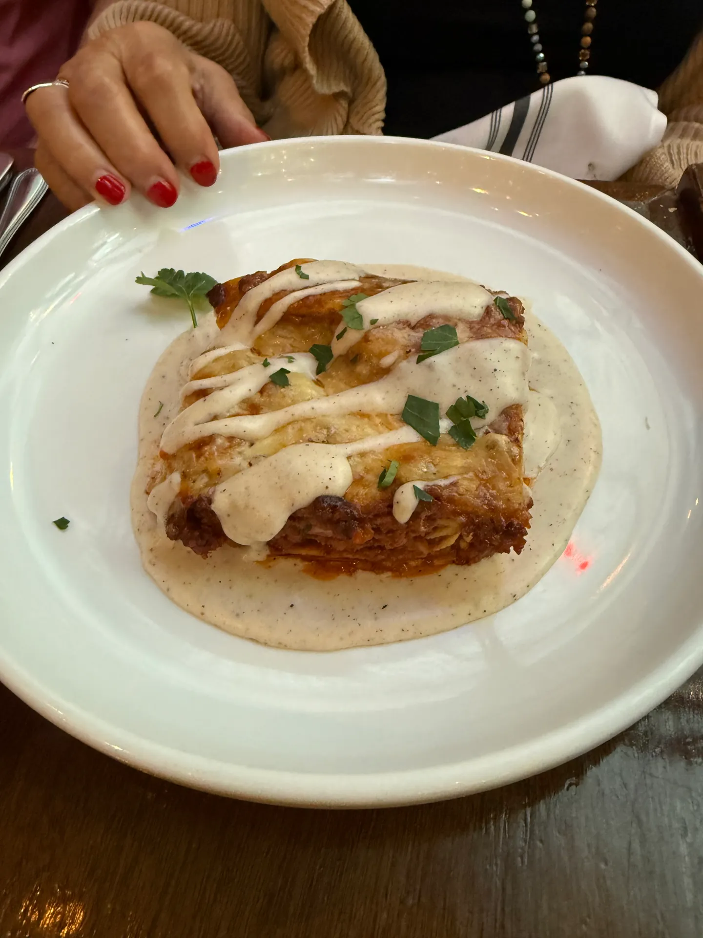 A slice of baked layered lasagna on a cream sauce topped with parsley.