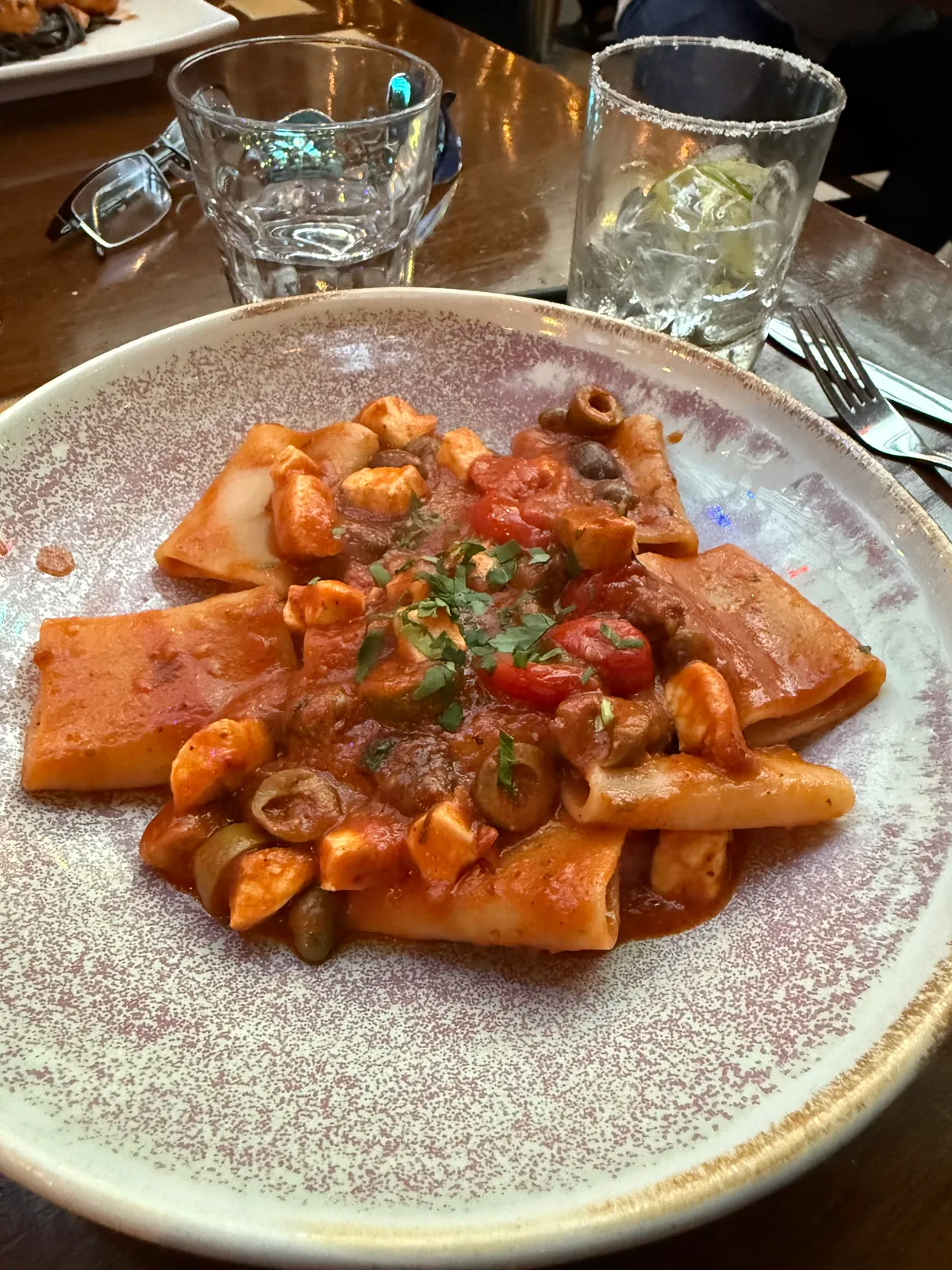 Wide paccheri pasta with swordfish, green olives, capers, and cherry tomatoes in tomato sauce.