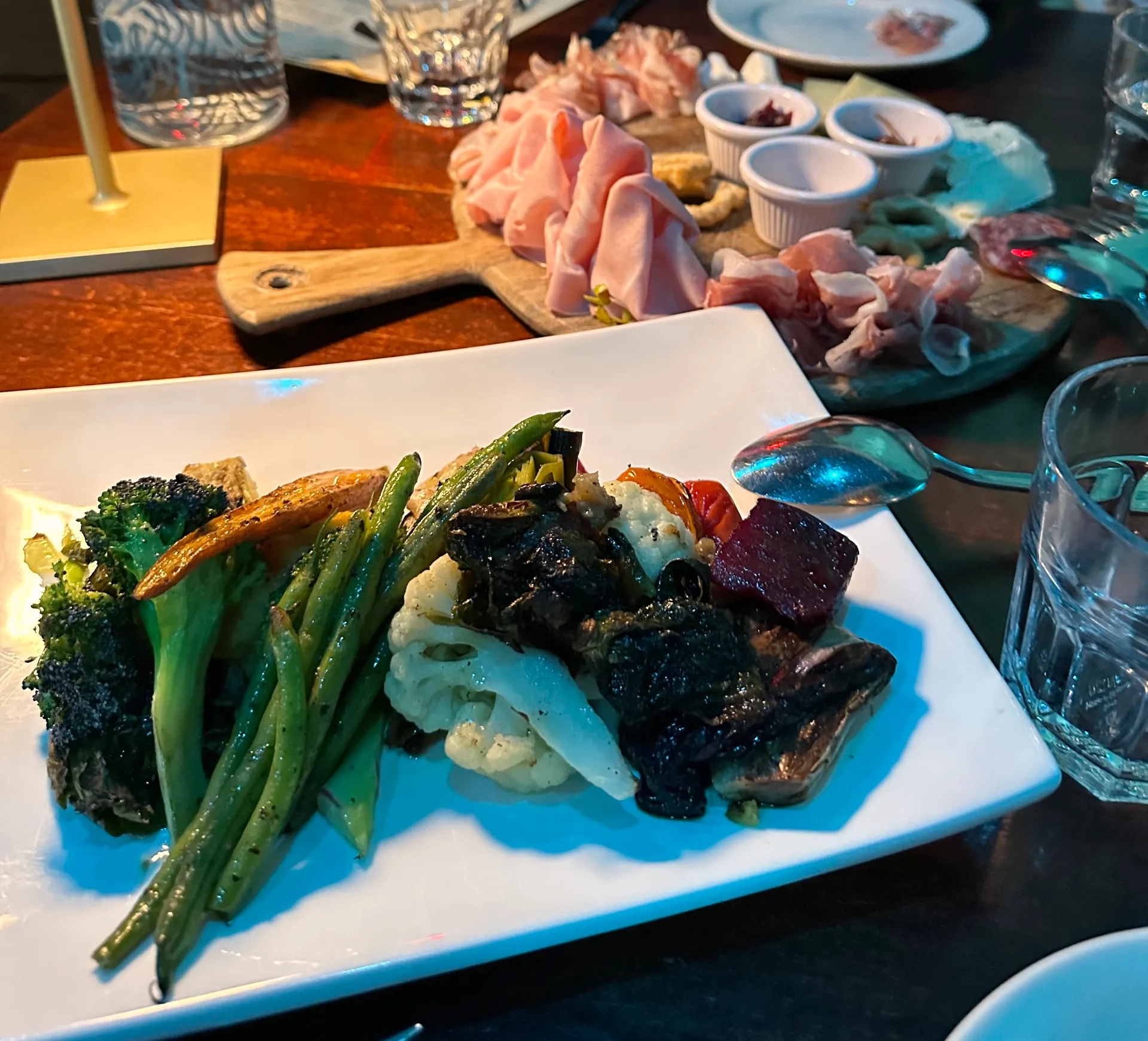 A wooden board of sliced cured meats and cheeses with small dishes of condiments.