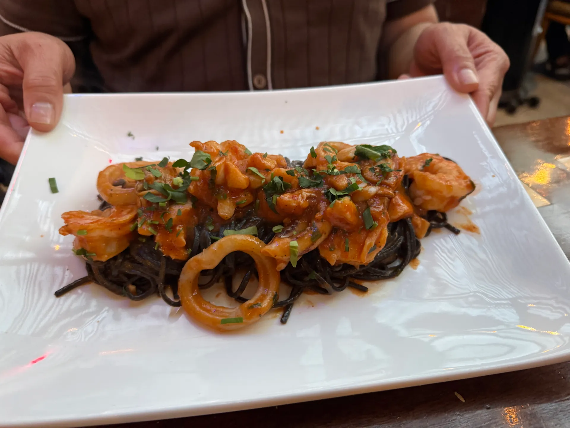Black squid-ink pasta with prawns and calamari rings in tomato sauce on a white plate.