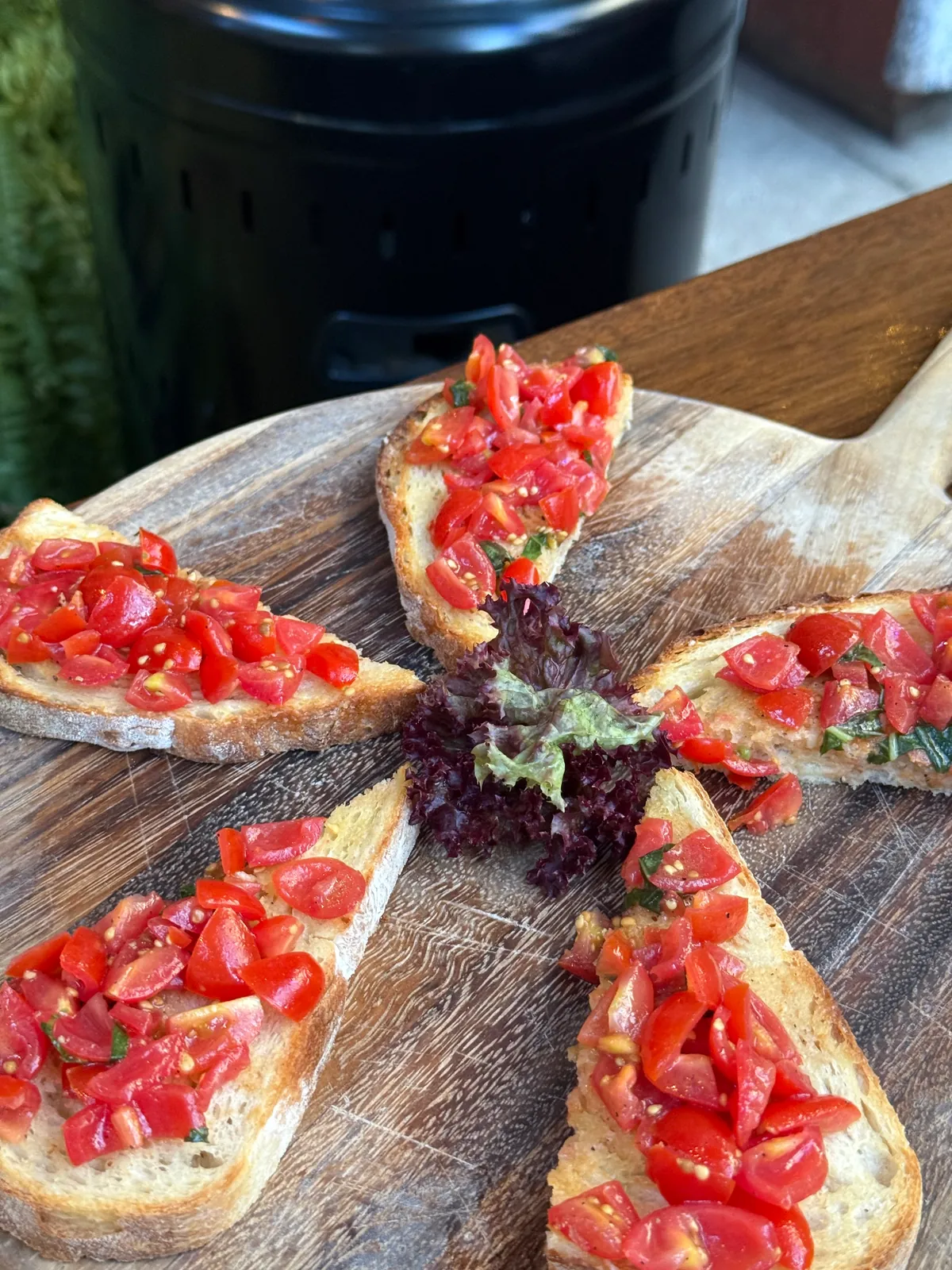 Grilled bread topped with chopped tomato and basil arranged on a wooden board.