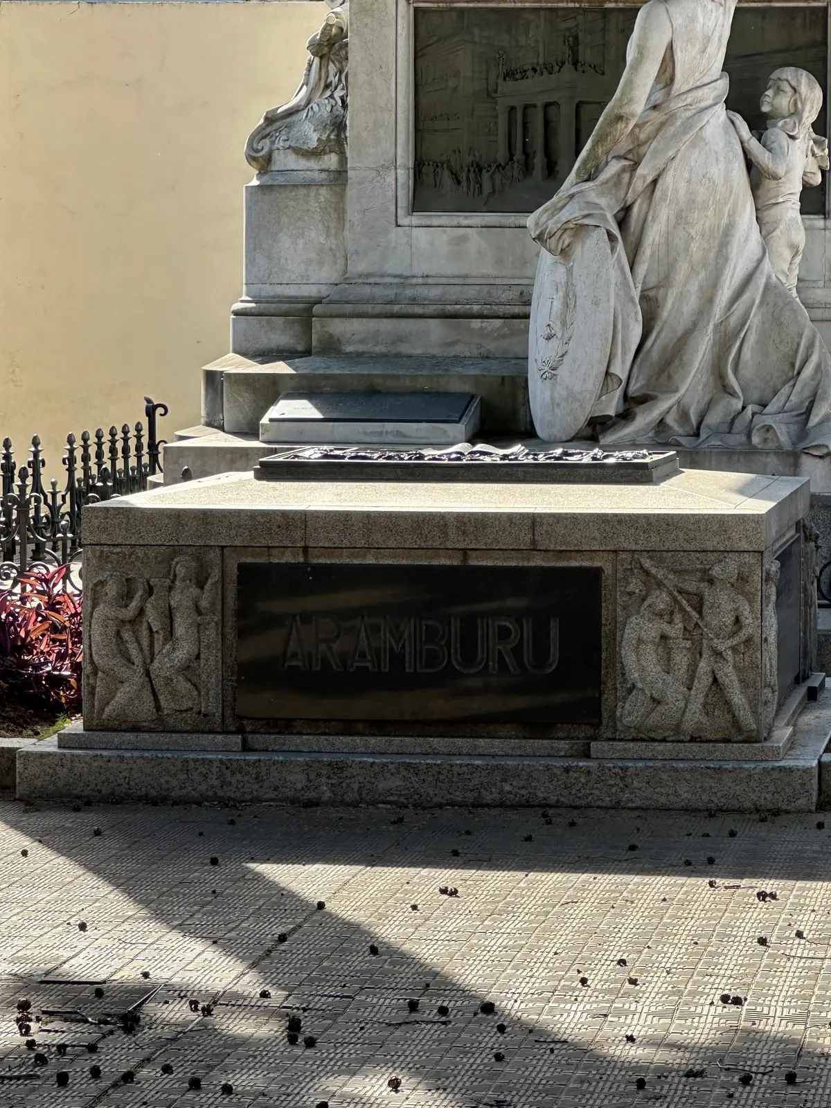 The plain granite tomb of Pedro Eugenio Aramburu below a marble group of mourning figures.