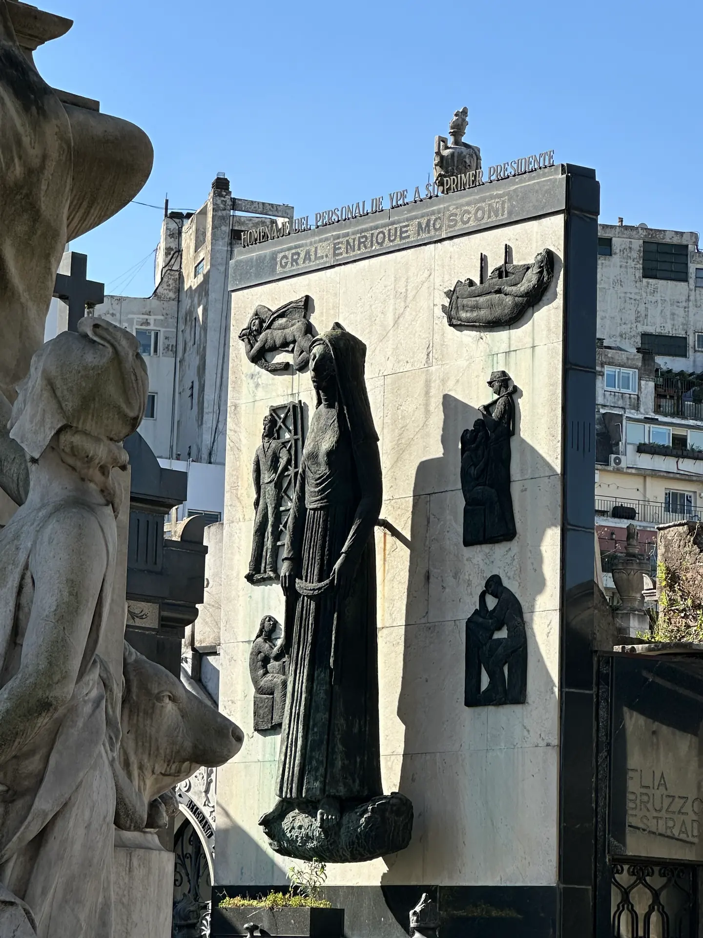 The monument to General Enrique Mosconi, a hooded bronze figure on a marble slab with relief panels.