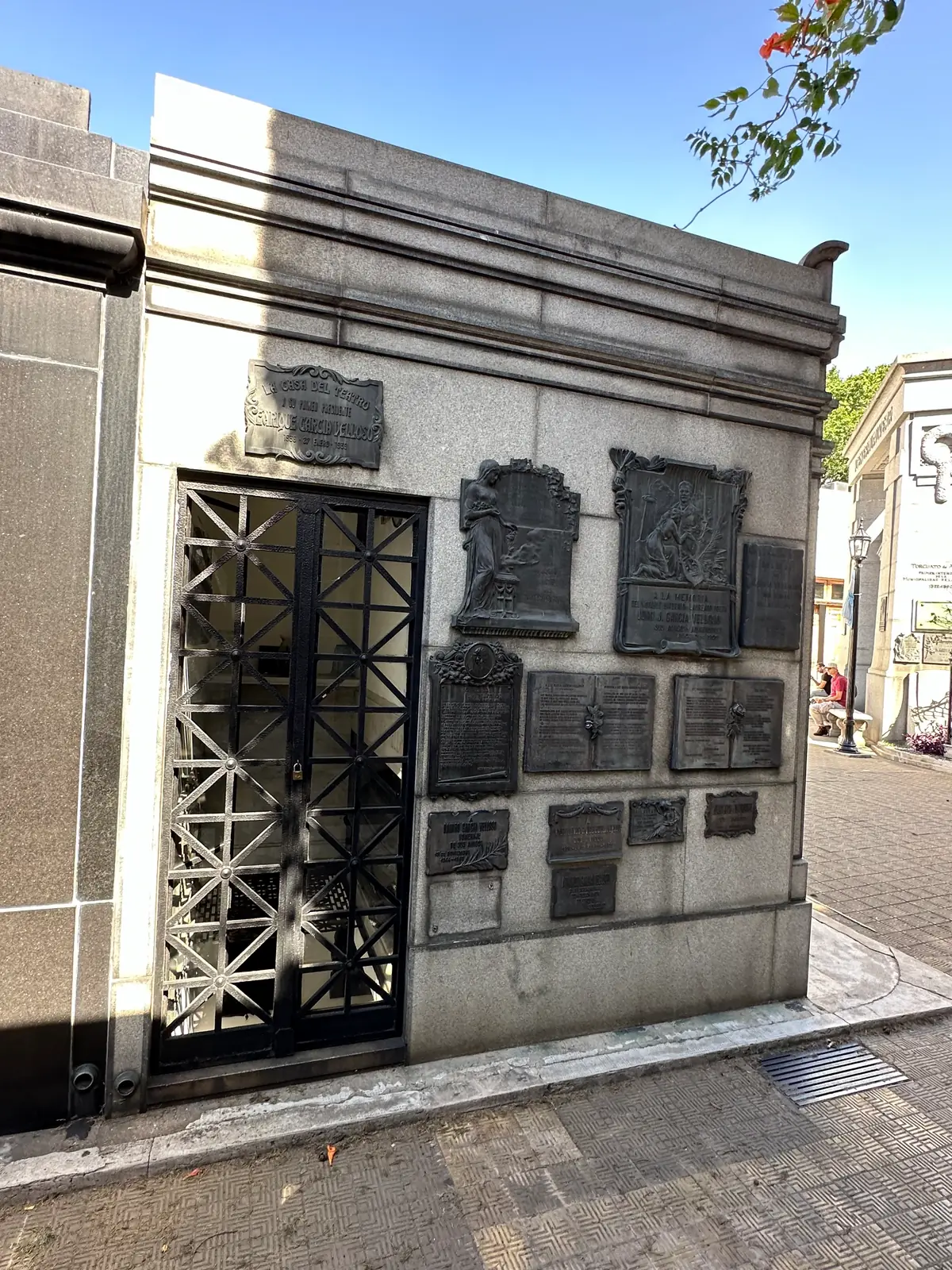 A Recoleta mausoleum with bronze memorial plaques beside an iron grille door.