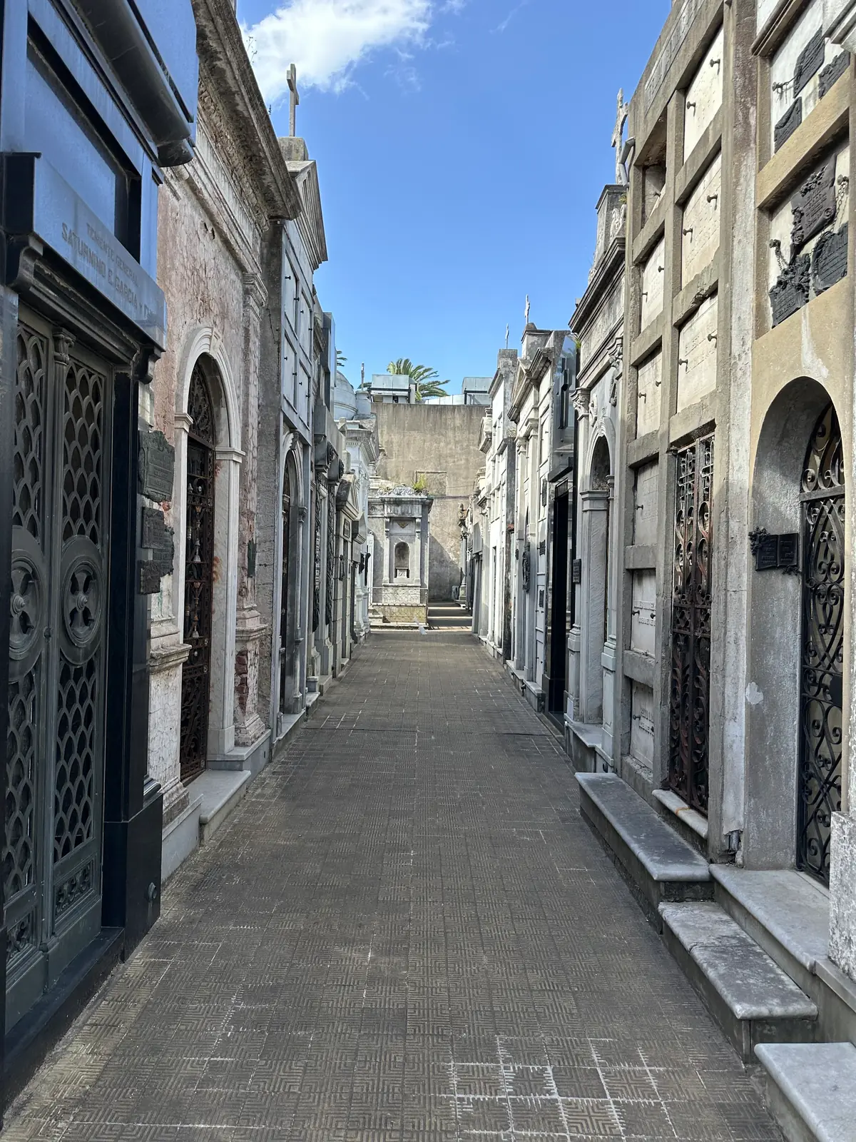 A narrow corridor of mausoleums in Recoleta Cemetery receding to a vanishing point.