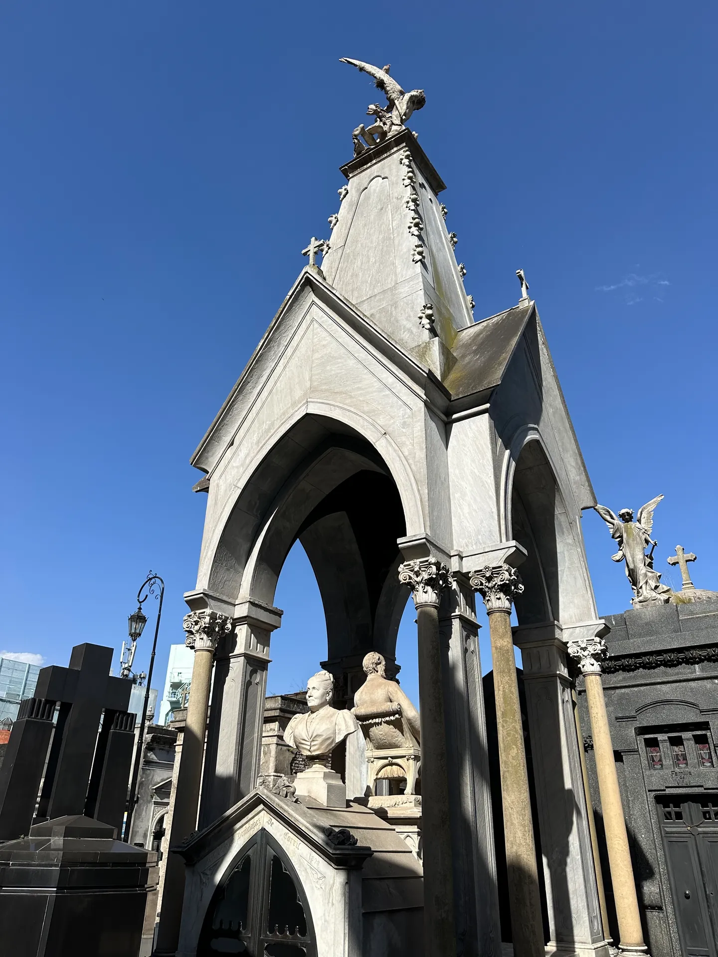 A gothic mausoleum with an angel finial and flanking statues against clear sky.