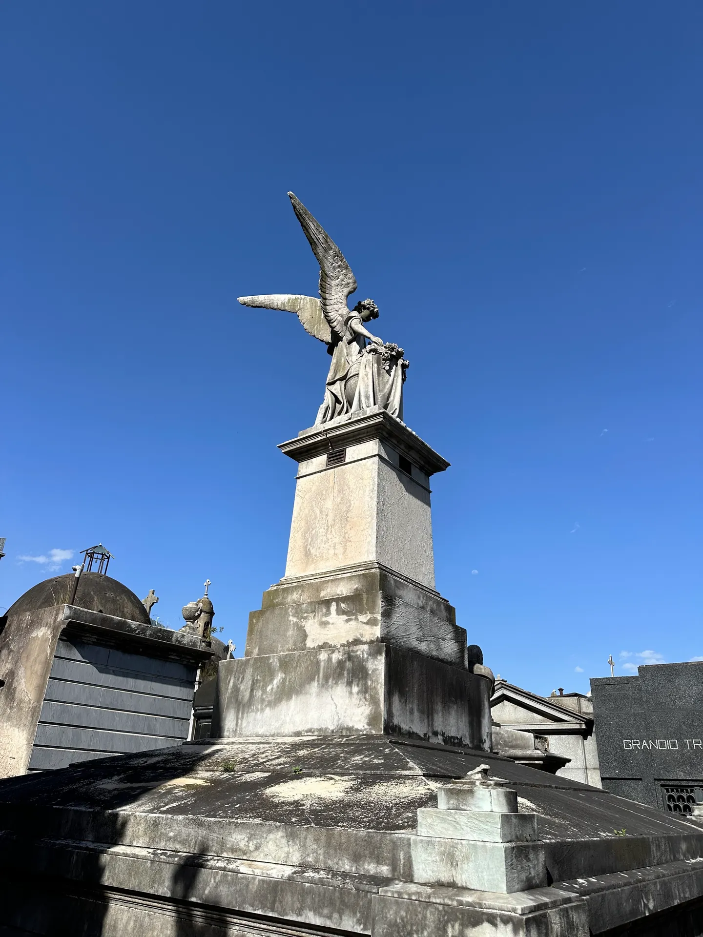 A winged marble angel on a plinth against clear sky in Recoleta Cemetery.