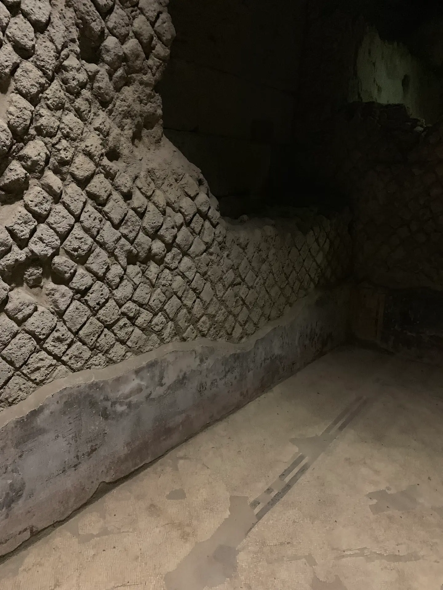 A paved Roman floor with a cut drainage channel below reticulate stone walling.