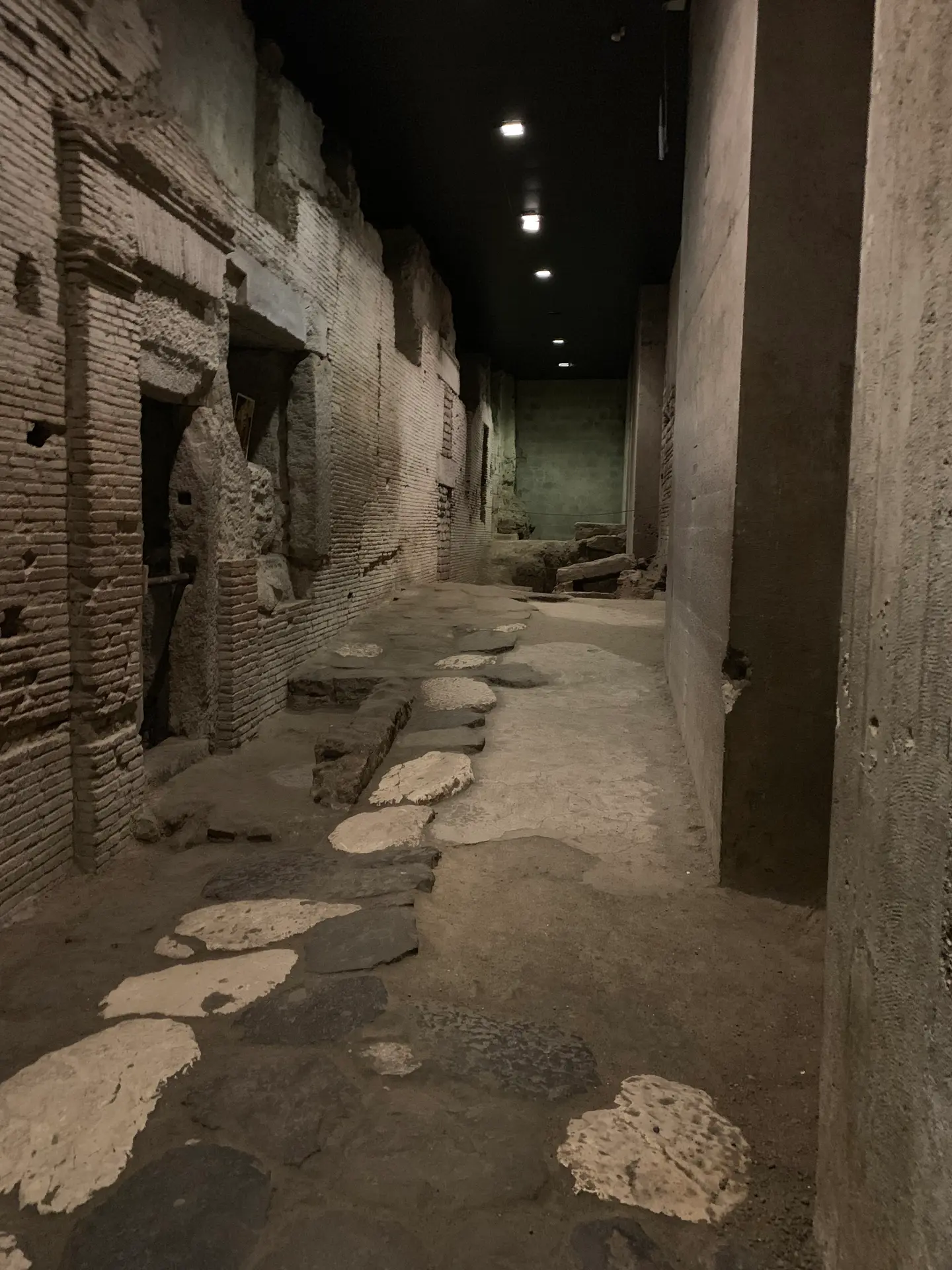 A paved Roman street with stone slabs running between excavated walls in Naples.
