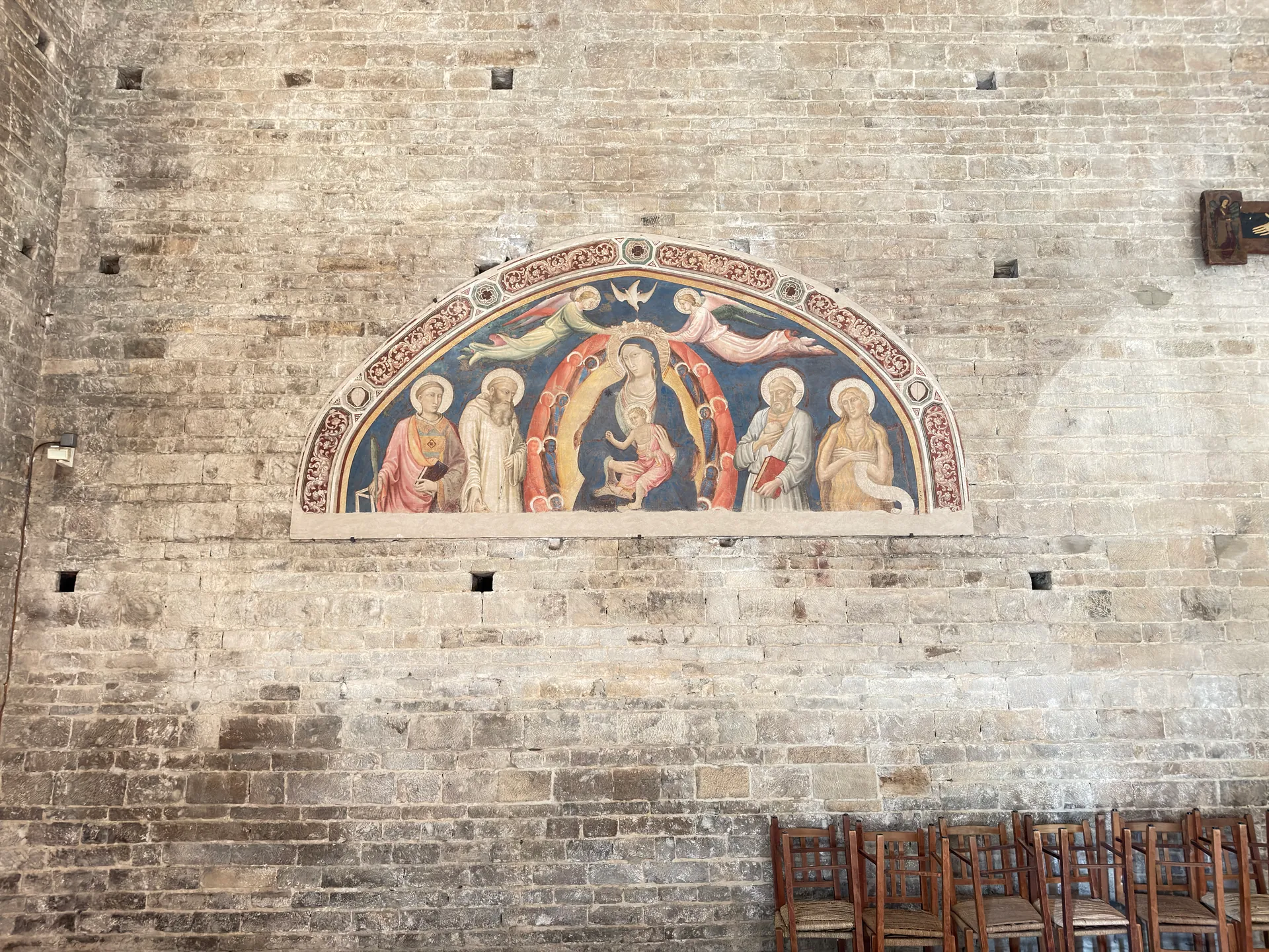 A detached fresco lunette sitting small on a great expanse of bare masonry in San Miniato.