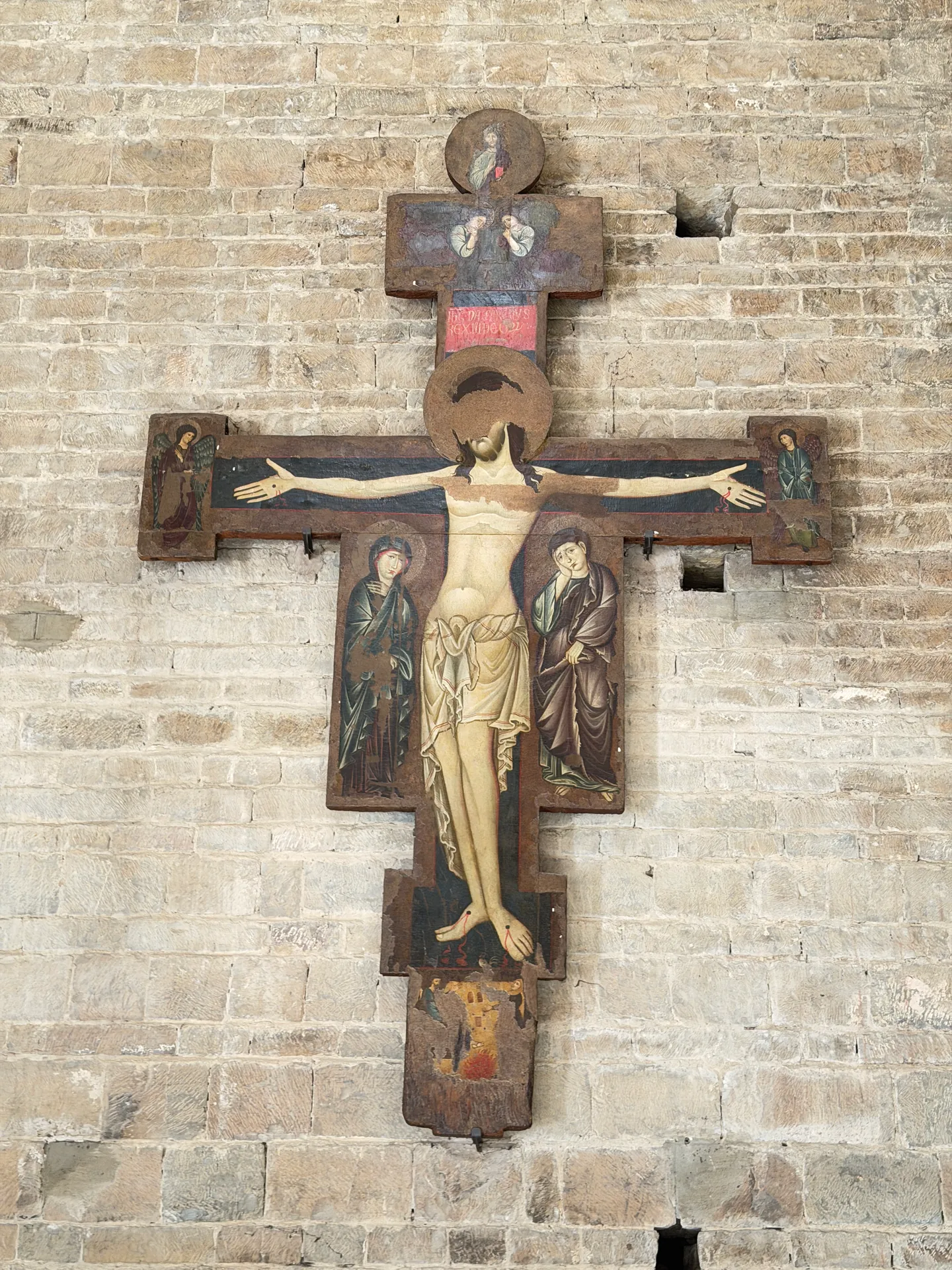 A painted crucifix hanging on the bare masonry of San Miniato's aisle wall.
