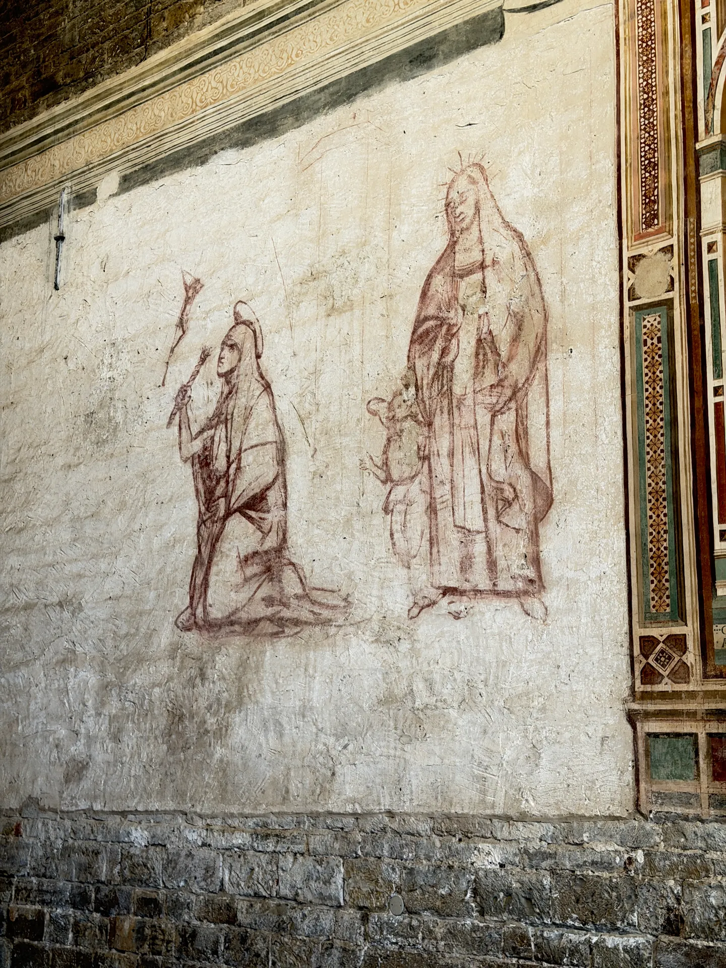 The red sinopia underdrawing of a lost fresco, exposed on the bare plaster of an aisle wall.
