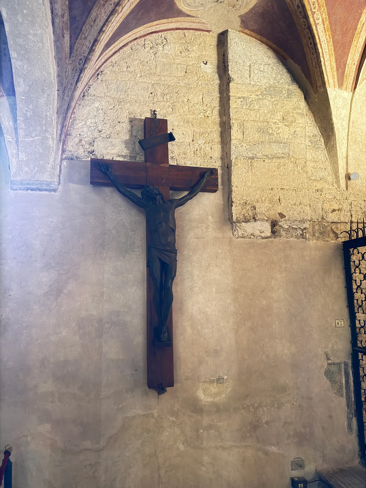 A wooden crucifix on the bare wall of San Miniato's crypt, under painted groin vaulting.