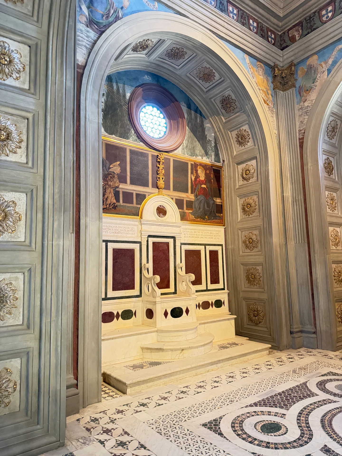The inlaid marble throne set against the wall of the Cardinal of Portugal's chapel, above the patterned pavement.