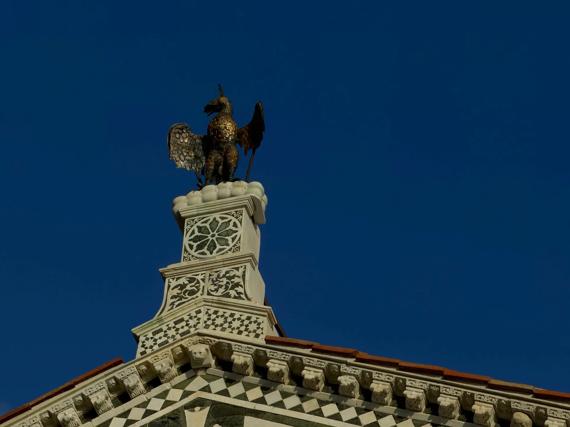 The bronze eagle of the Arte di Calimala on its marble pedestal at the apex of the facade.