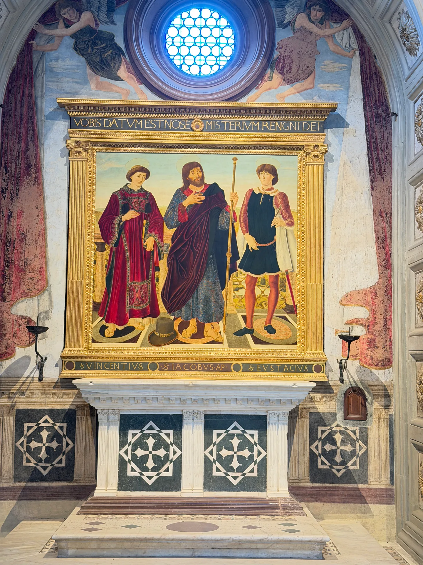 The altar wall of the Cardinal of Portugal's chapel, three standing saints in a gilded frame below a pierced oculus.