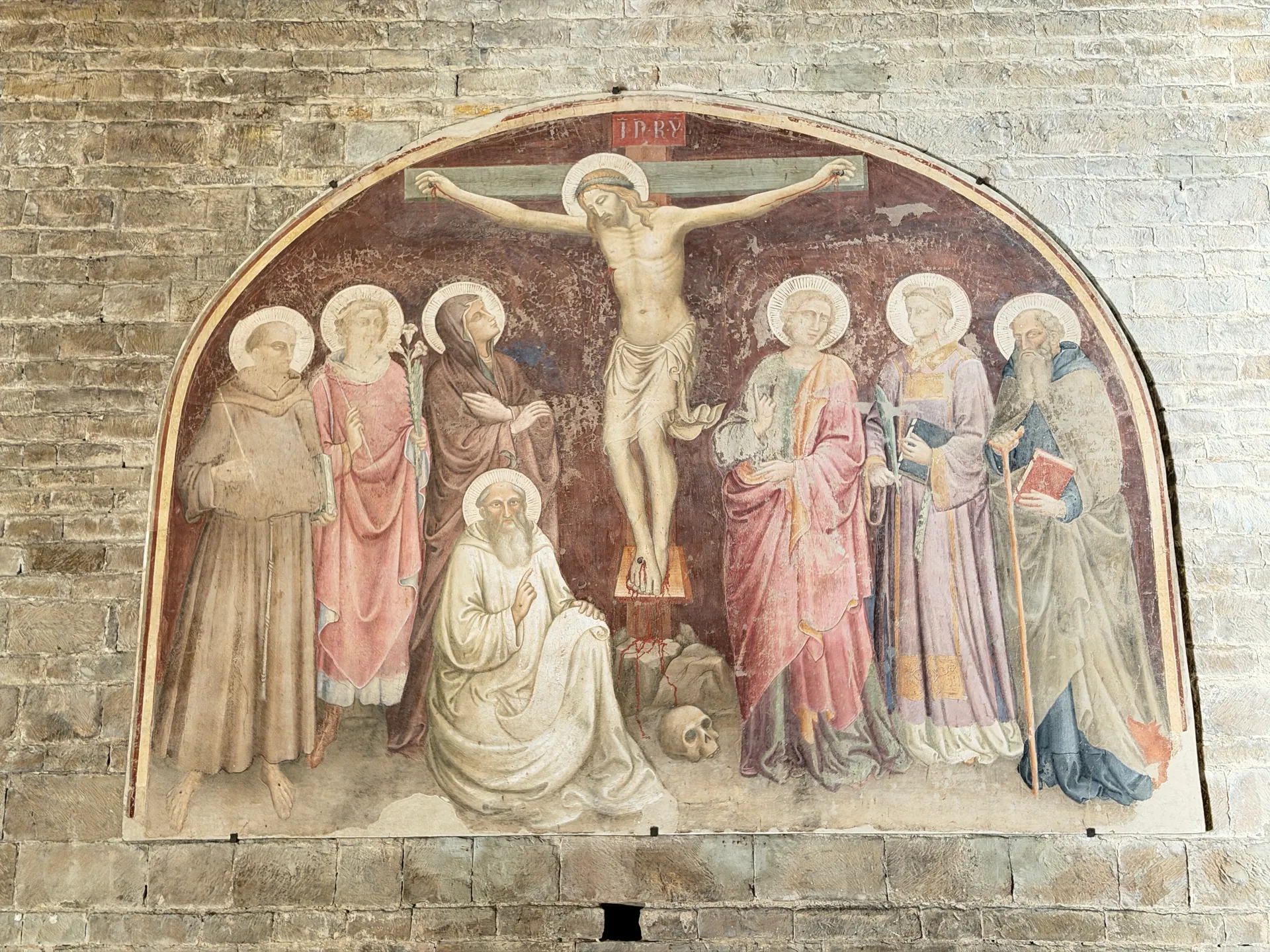 A detached Crucifixion lunette on the bare stone wall of San Miniato, Christ among saints with a kneeling monk.
