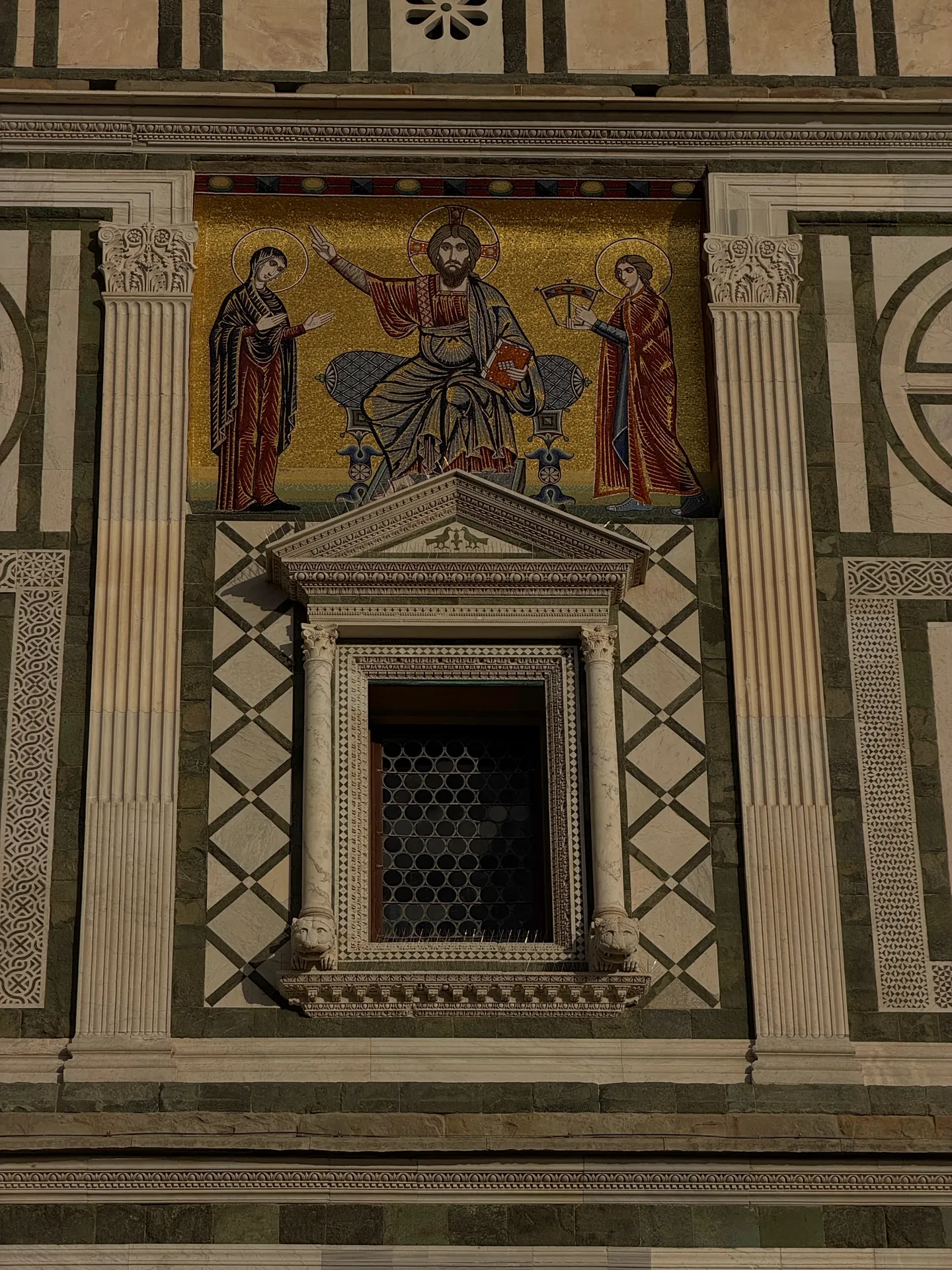 The facade mosaic of San Miniato, Christ enthroned between two figures, set in the marble geometry of the wall.