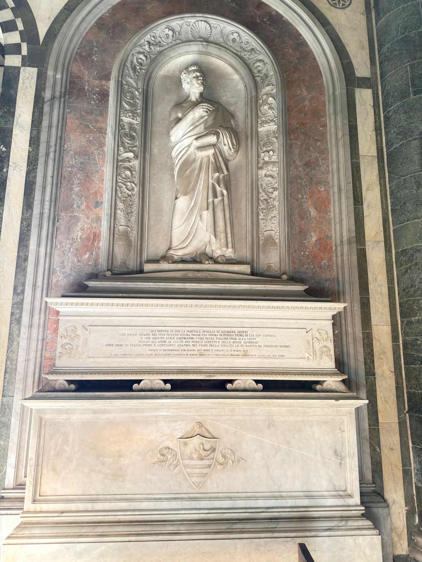 A nineteenth century wall monument at San Miniato, a standing figure in an arched niche above an inscribed sarcophagus.
