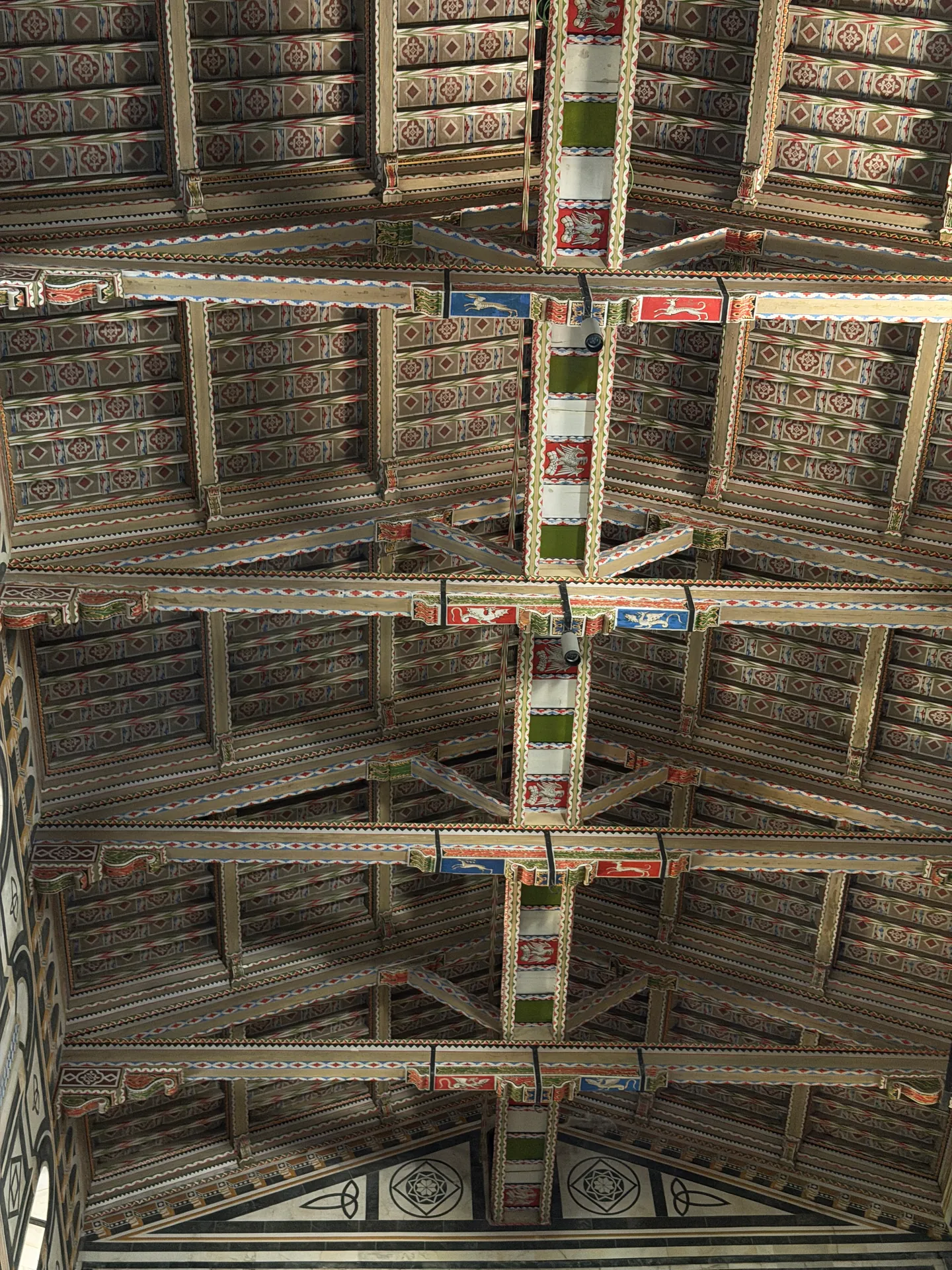 The painted open timber roof of San Miniato seen from the nave floor.