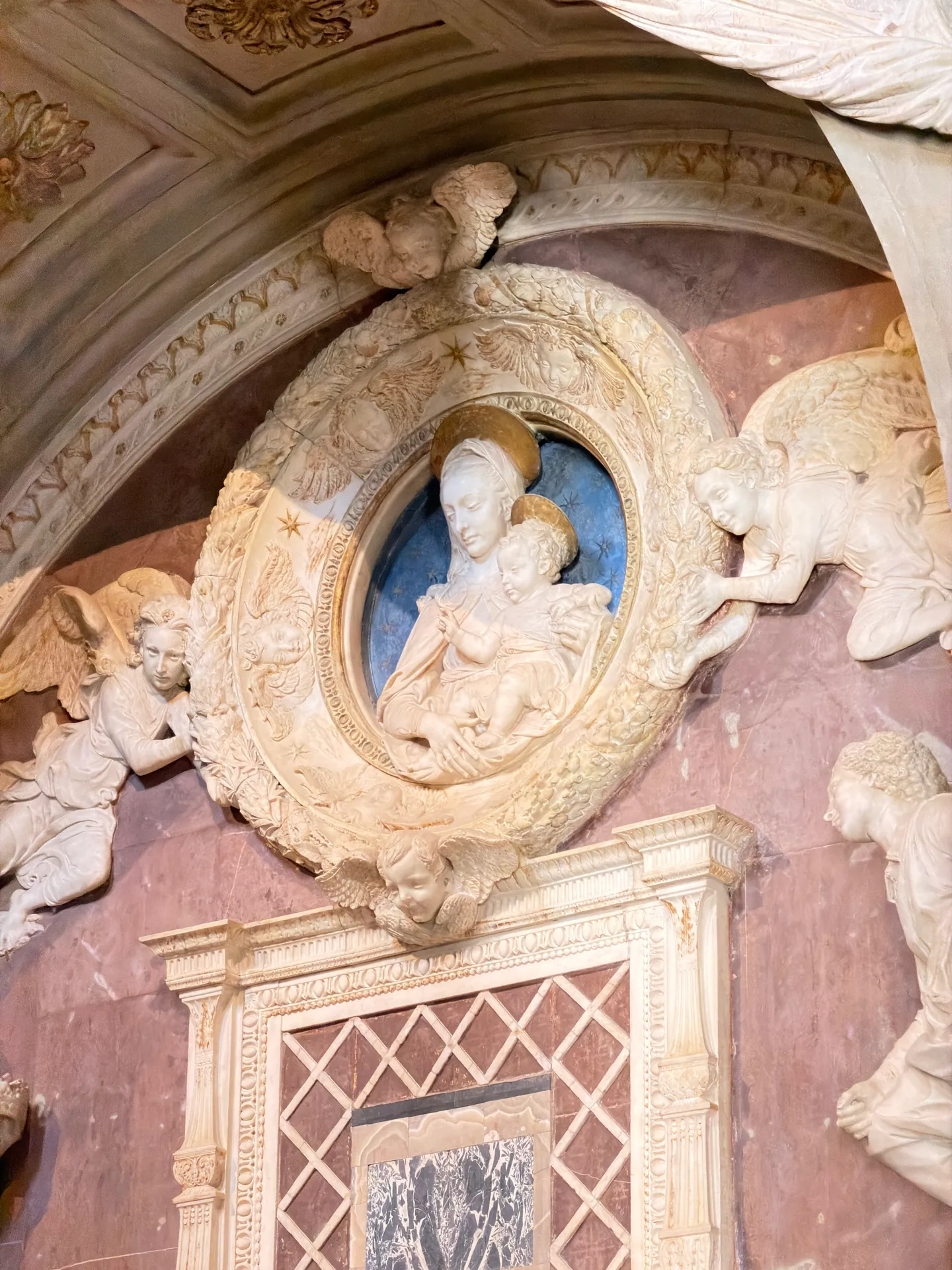 A white marble tondo of the Madonna and Child borne by two flying angels, part of Rossellino's monument.