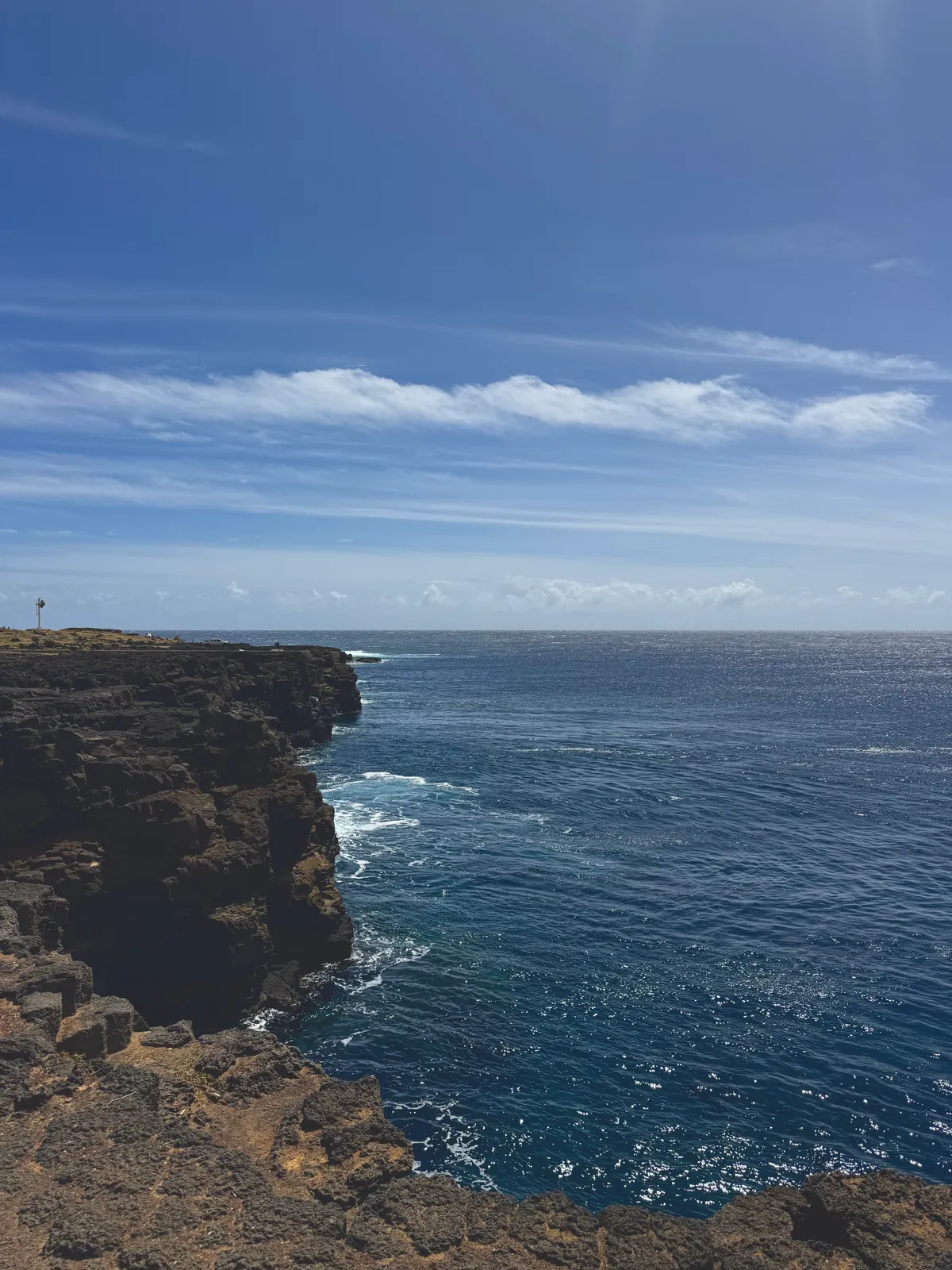 A dark lava cliff dropping into deep blue water at Ka Lae, the southern point of Hawaii Island