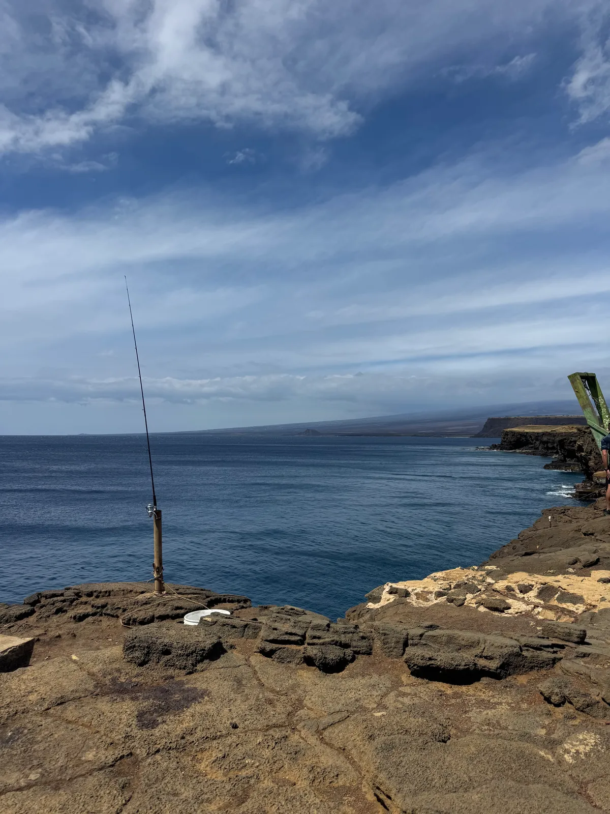 A fishing rod propped upright on lava rock at the edge of a cliff above the sea