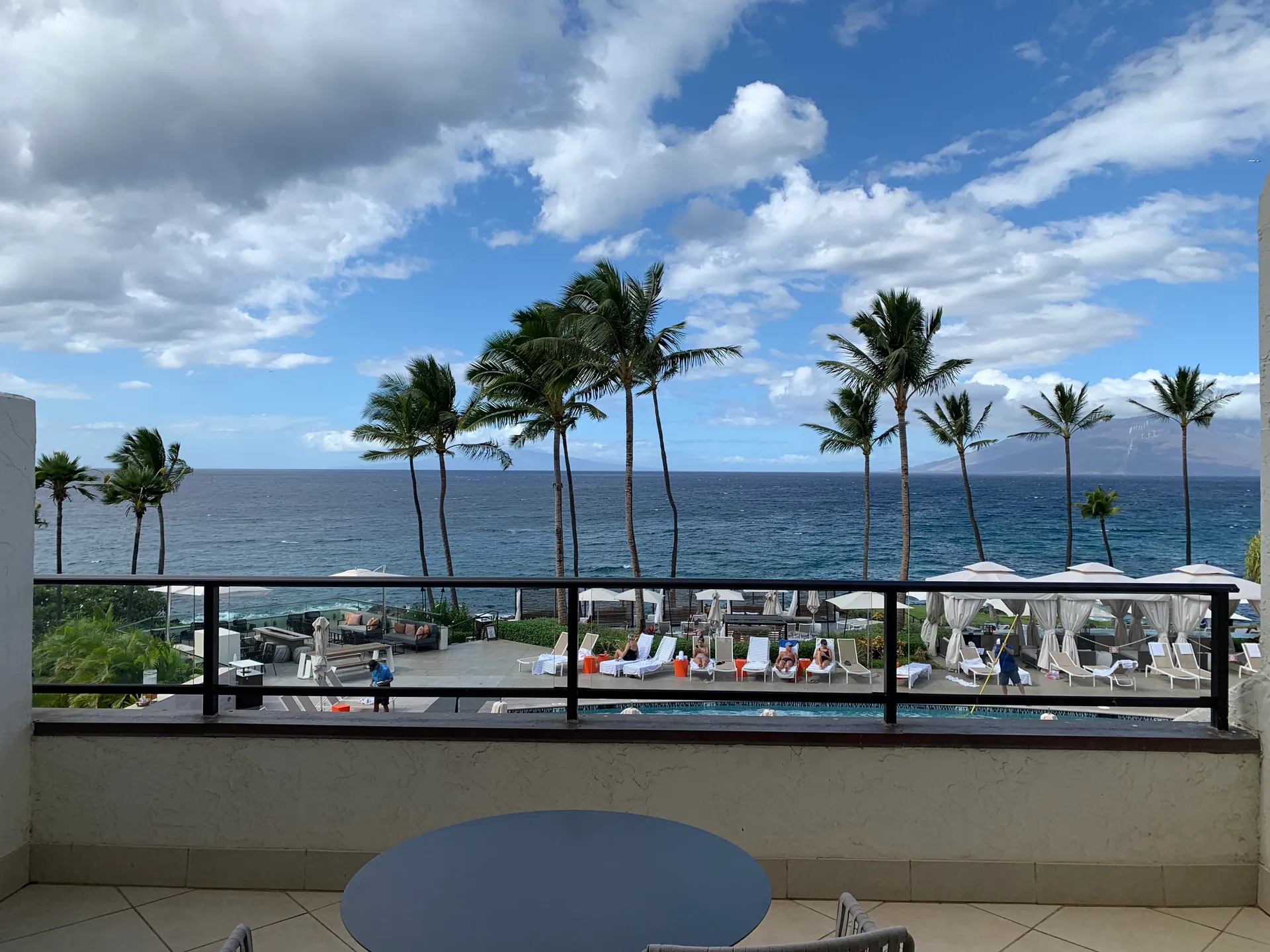 View from a balcony over a resort pool deck to palms and the ocean