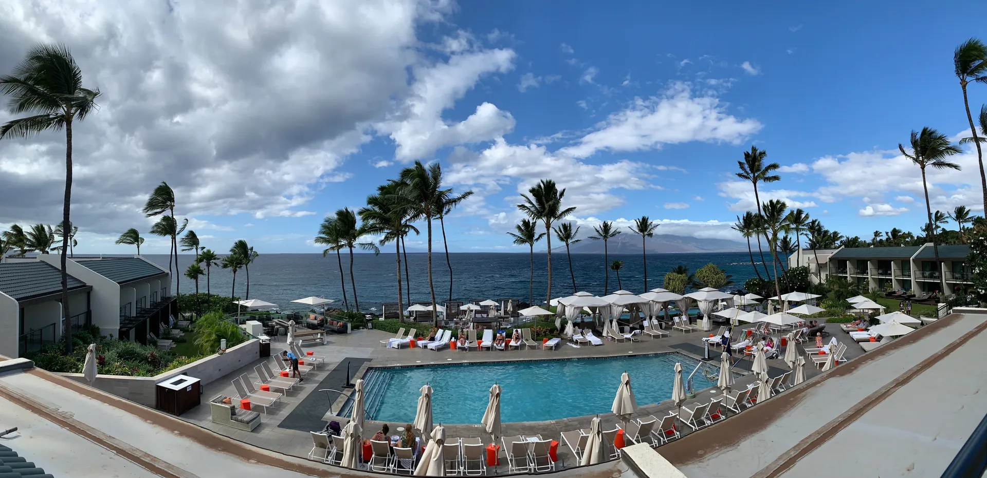 Resort pool and loungers seen from above with palms and ocean beyond
