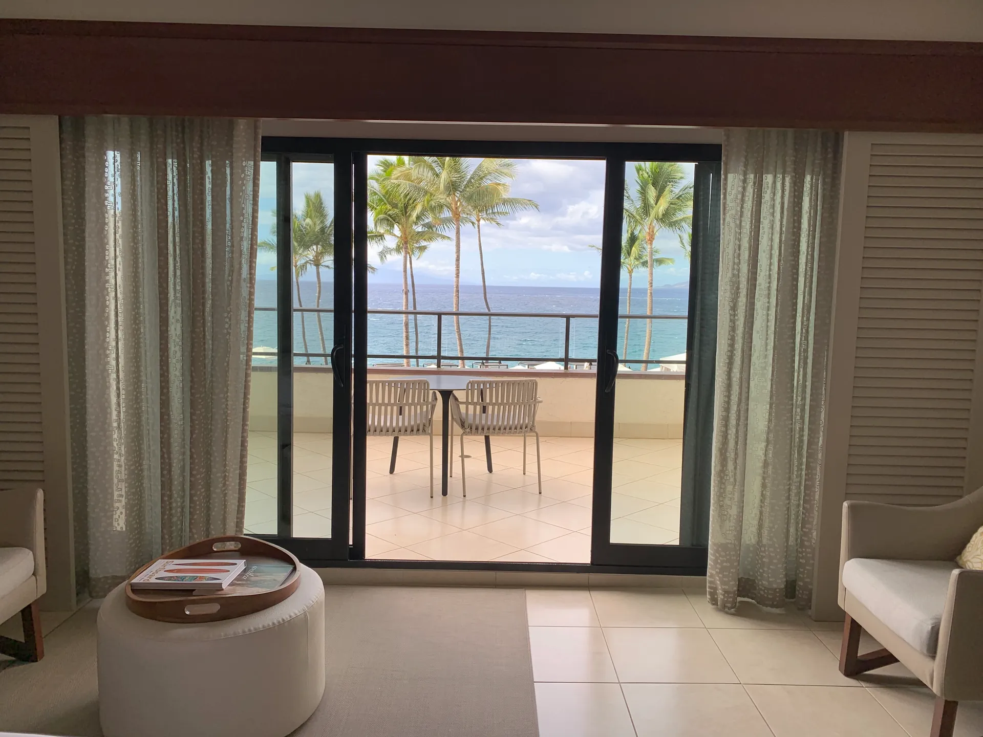 Hotel room looking through open doors to a lanai with chairs and palms