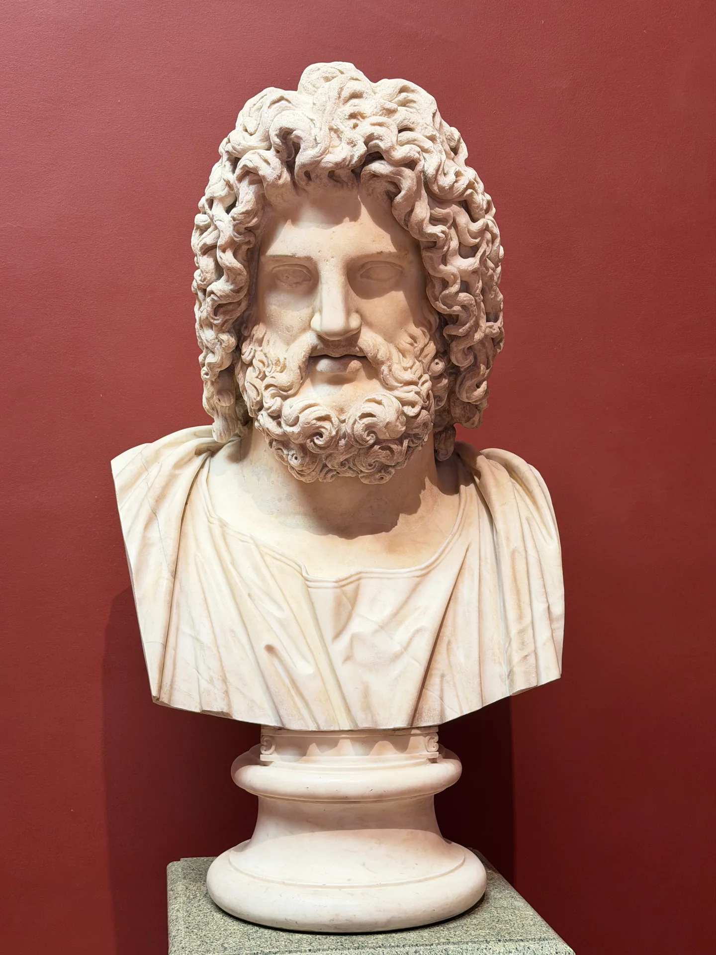 A colossal bearded marble head on its socle against the deep red wall of the Gabinetto dei Marmi.