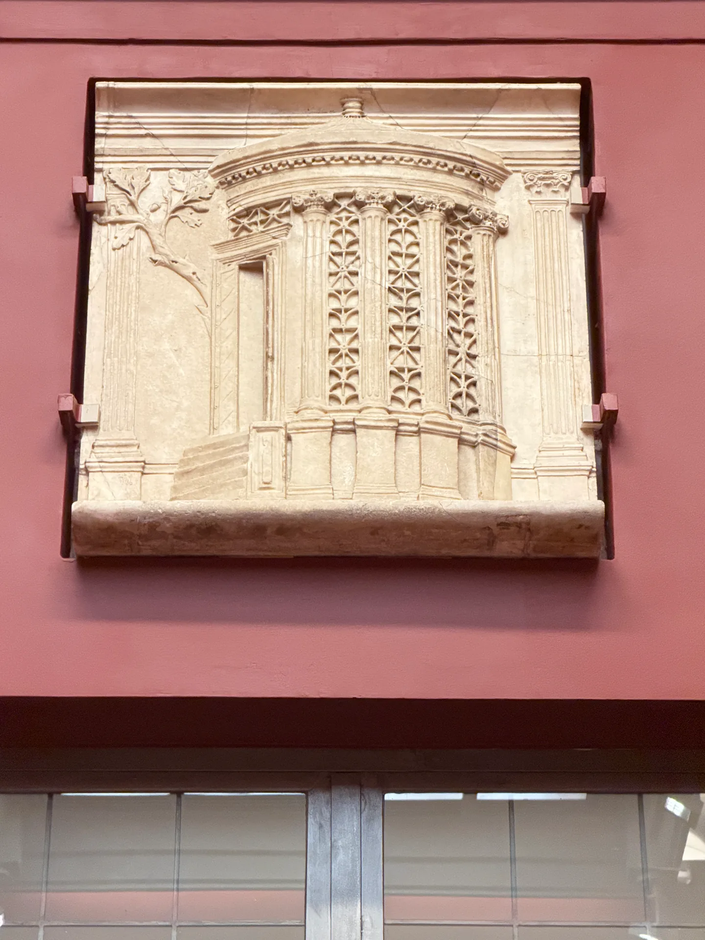 A marble relief panel carved with a miniature colonnaded facade, mounted on brackets.