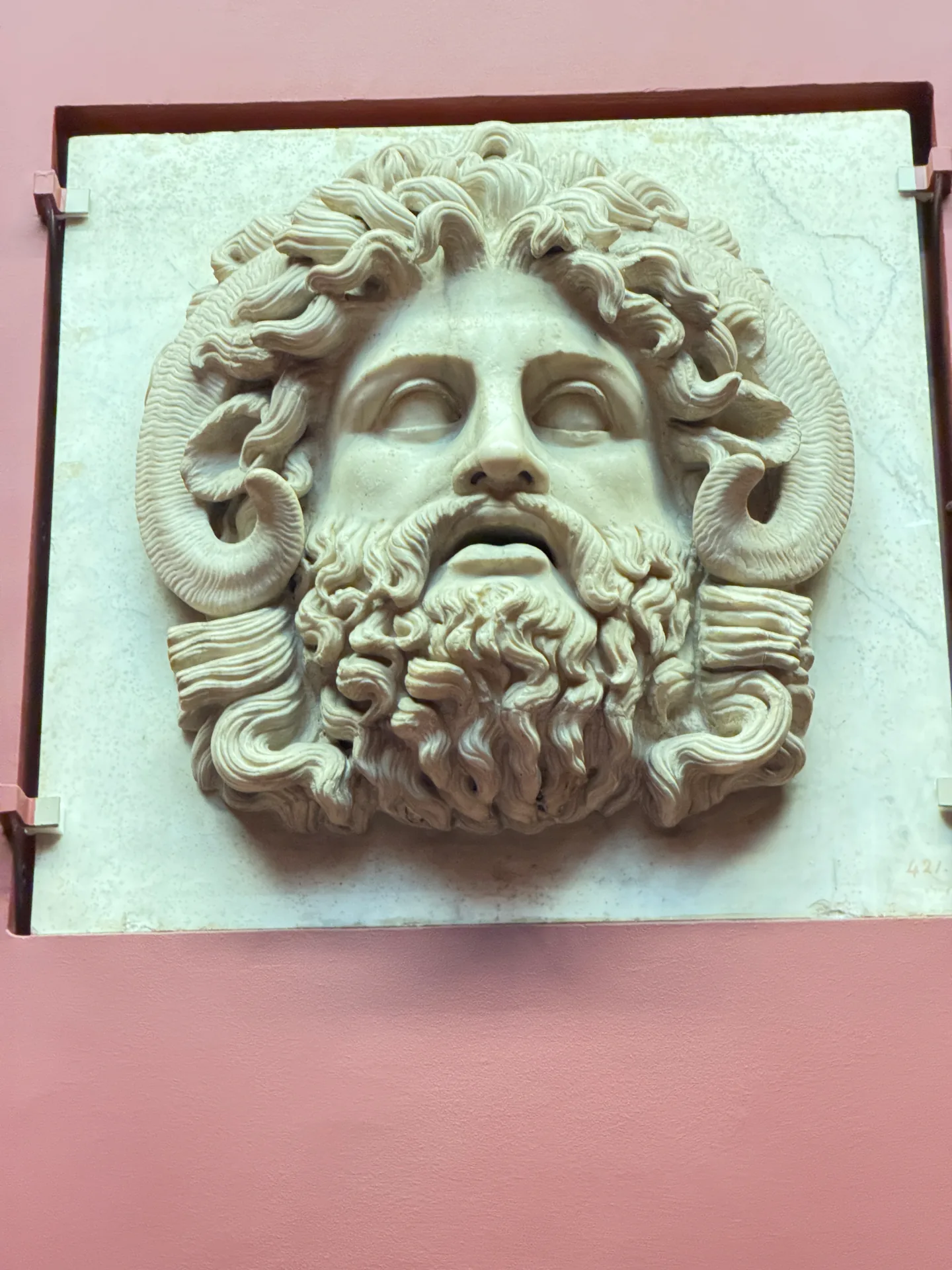 A marble mask of a bearded head with ram's horns curling behind the ears, mounted on the wall.