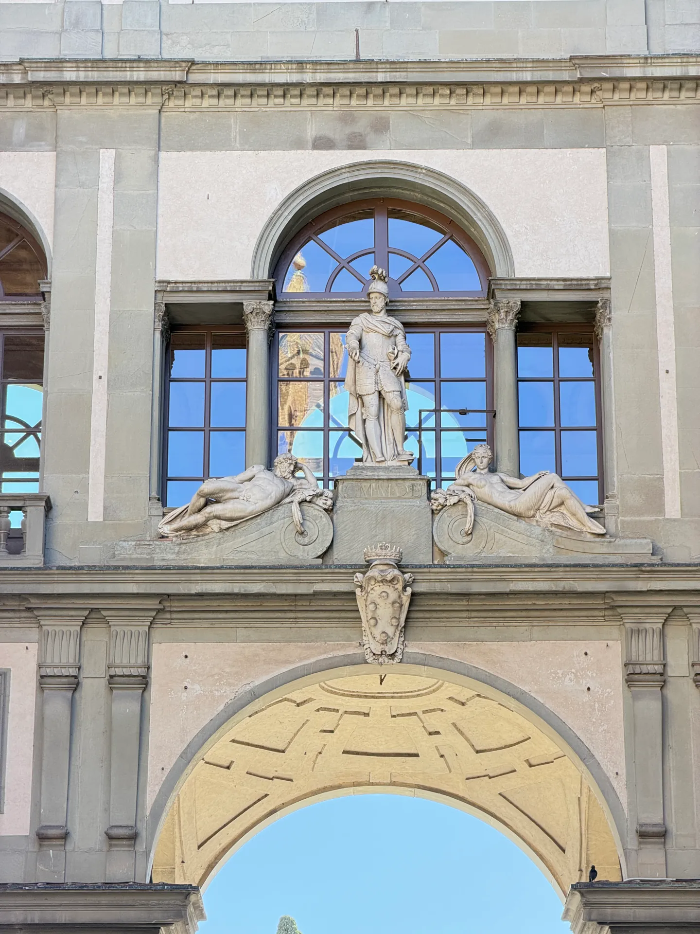 A marble figure set in the wall above the Uffizi courtyard arch, against open sky.