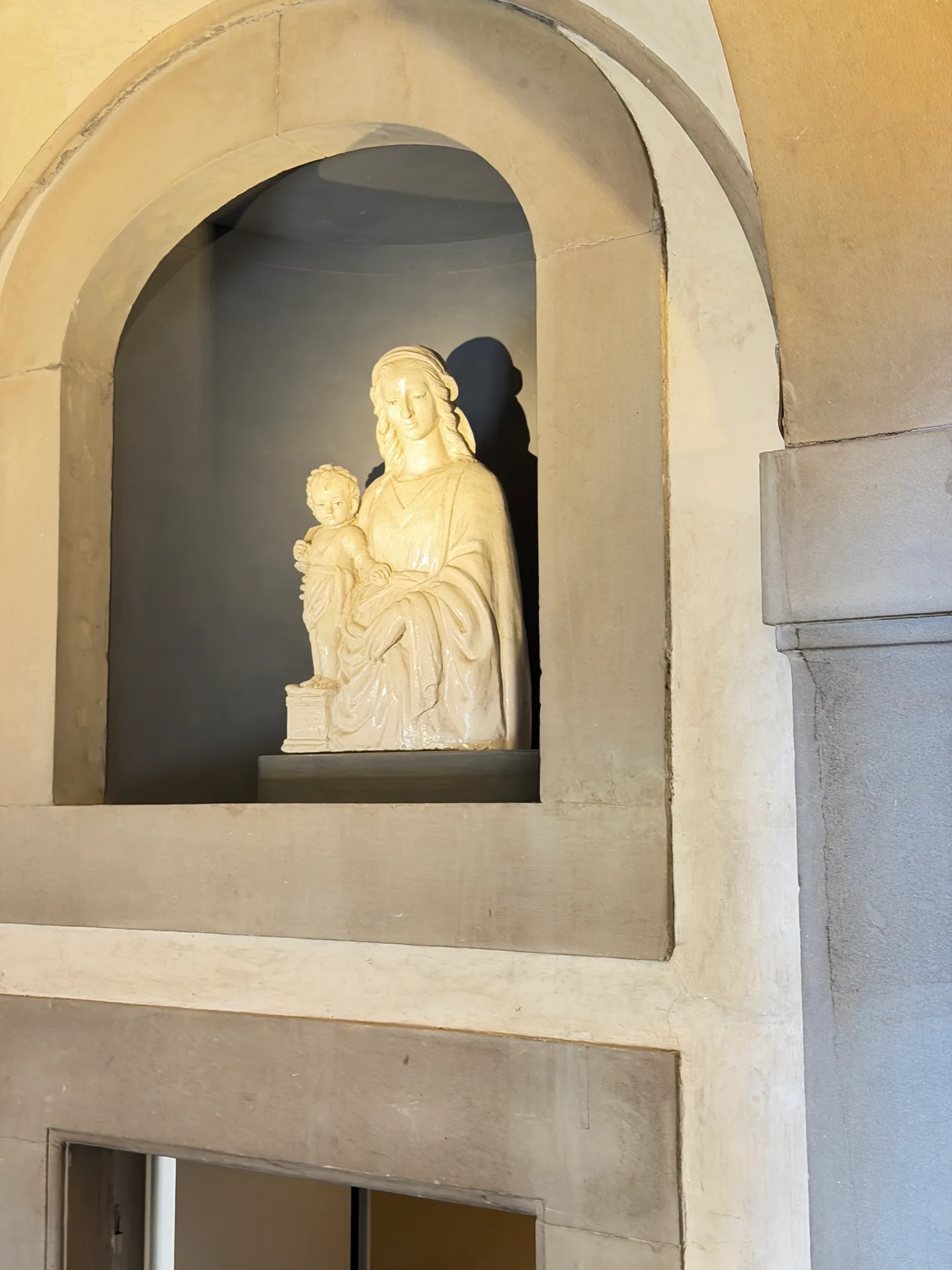 A marble Madonna and Child seated in a plain stone niche on a stairwell wall of the Uffizi.