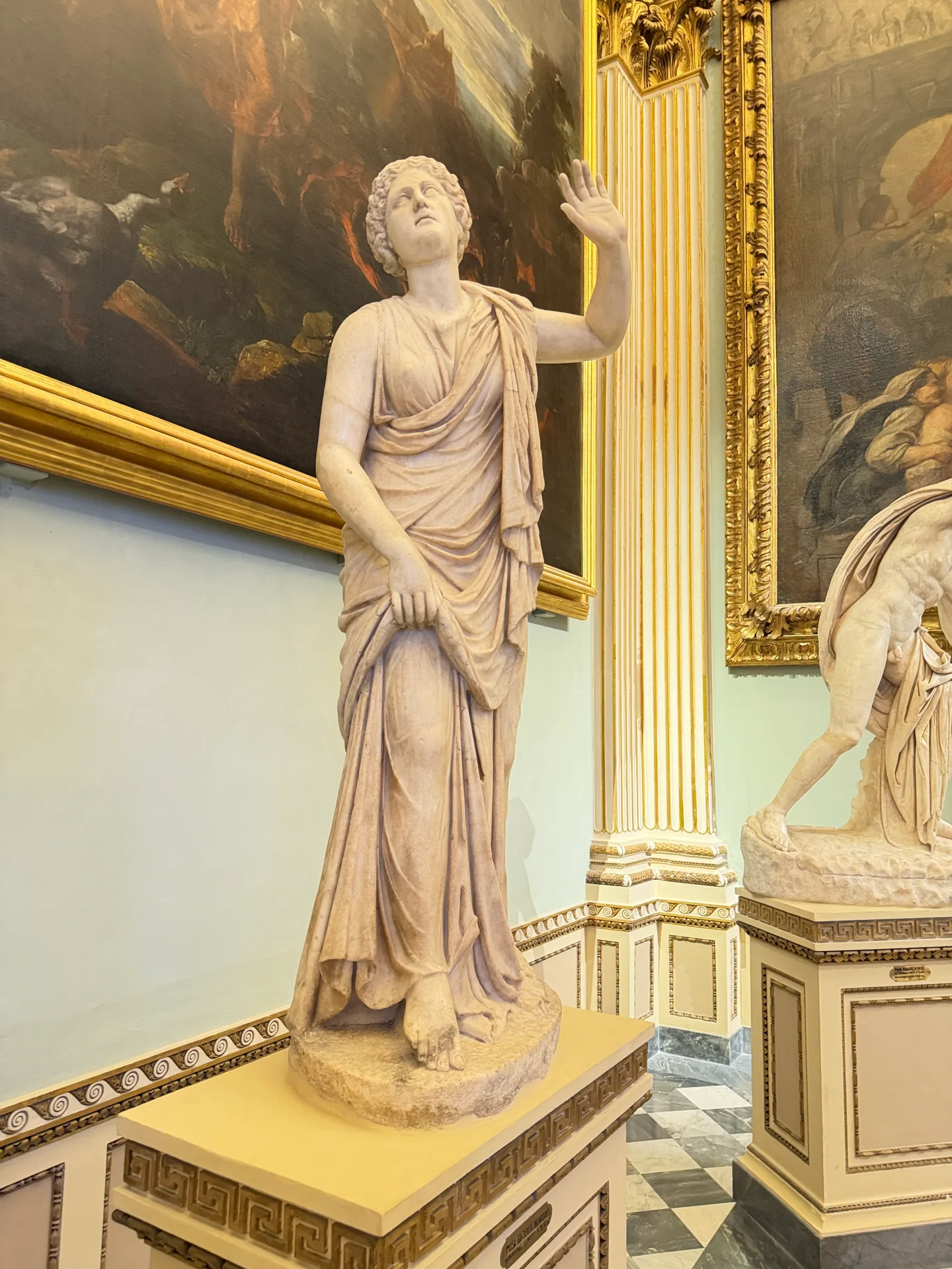 A standing draped daughter of Niobe, the pale marble clear against the wall behind.