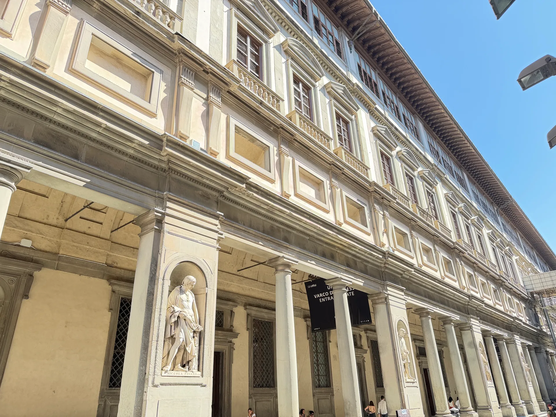 The east wing of the Uffizi courtyard in low raking sun, columns and statue niches receding toward the Arno.