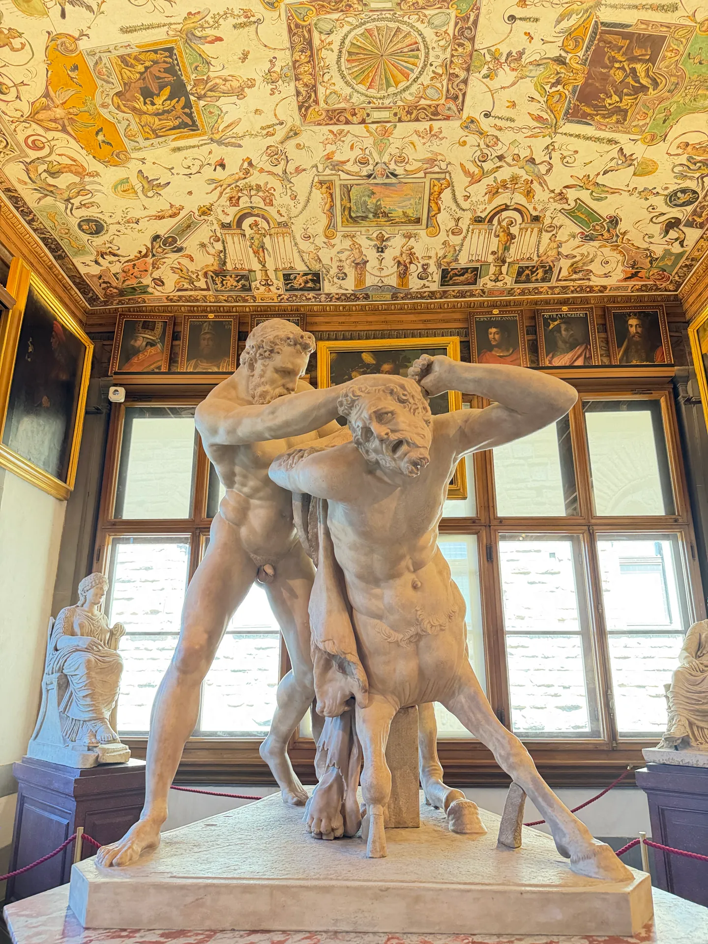The restored antique marble of Hercules and the centaur Nessus, on a red pedestal under a grotesque painted ceiling.