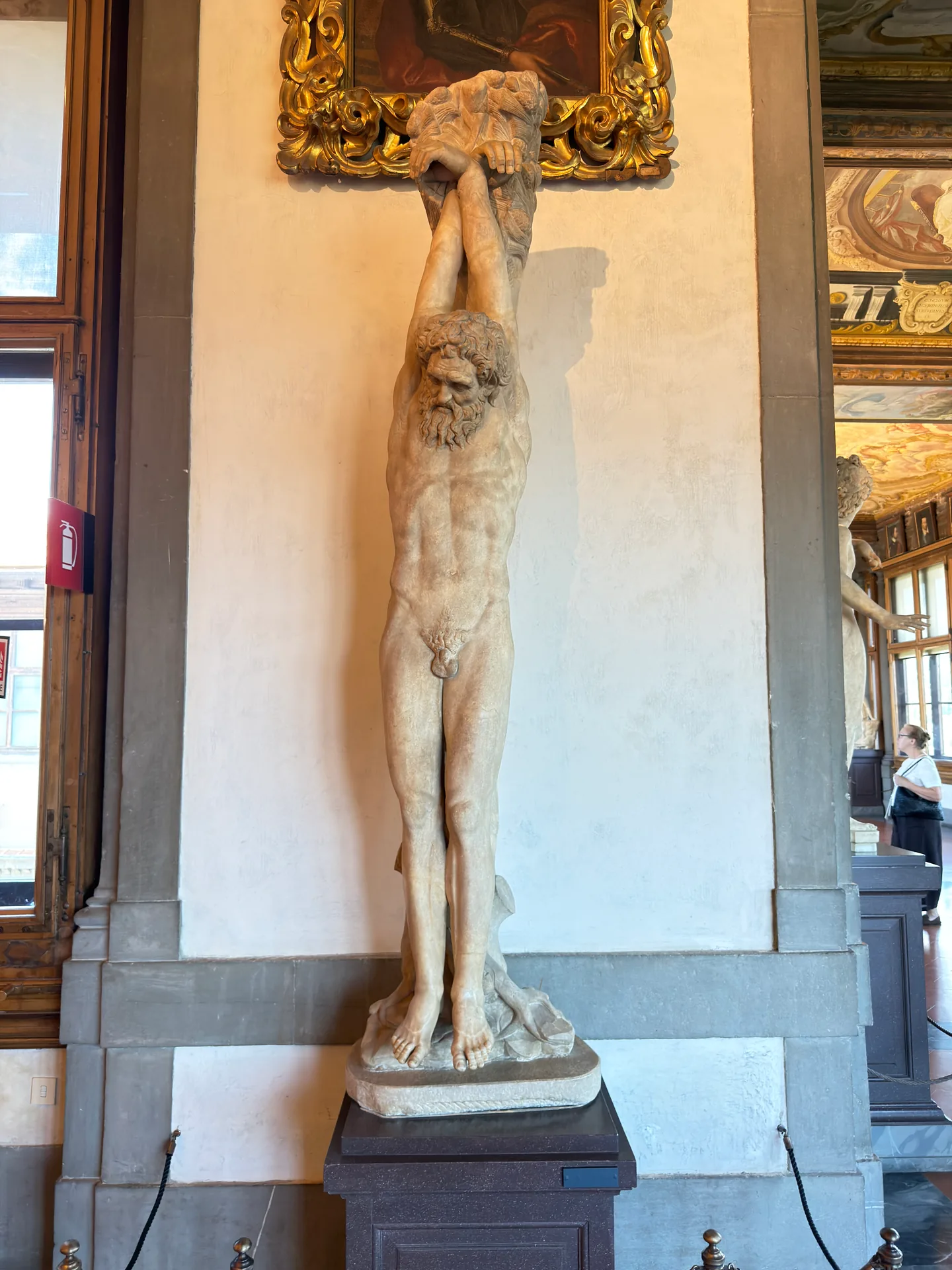 An antique marble of Marsyas strung up by the wrists, standing against a pier of the Uffizi corridor.