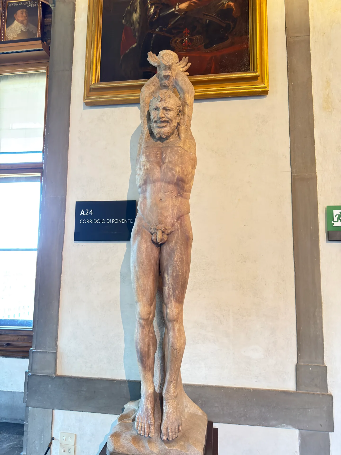The companion Marsyas of the pair, its stone deep red brown, against a corridor pier of the Uffizi.